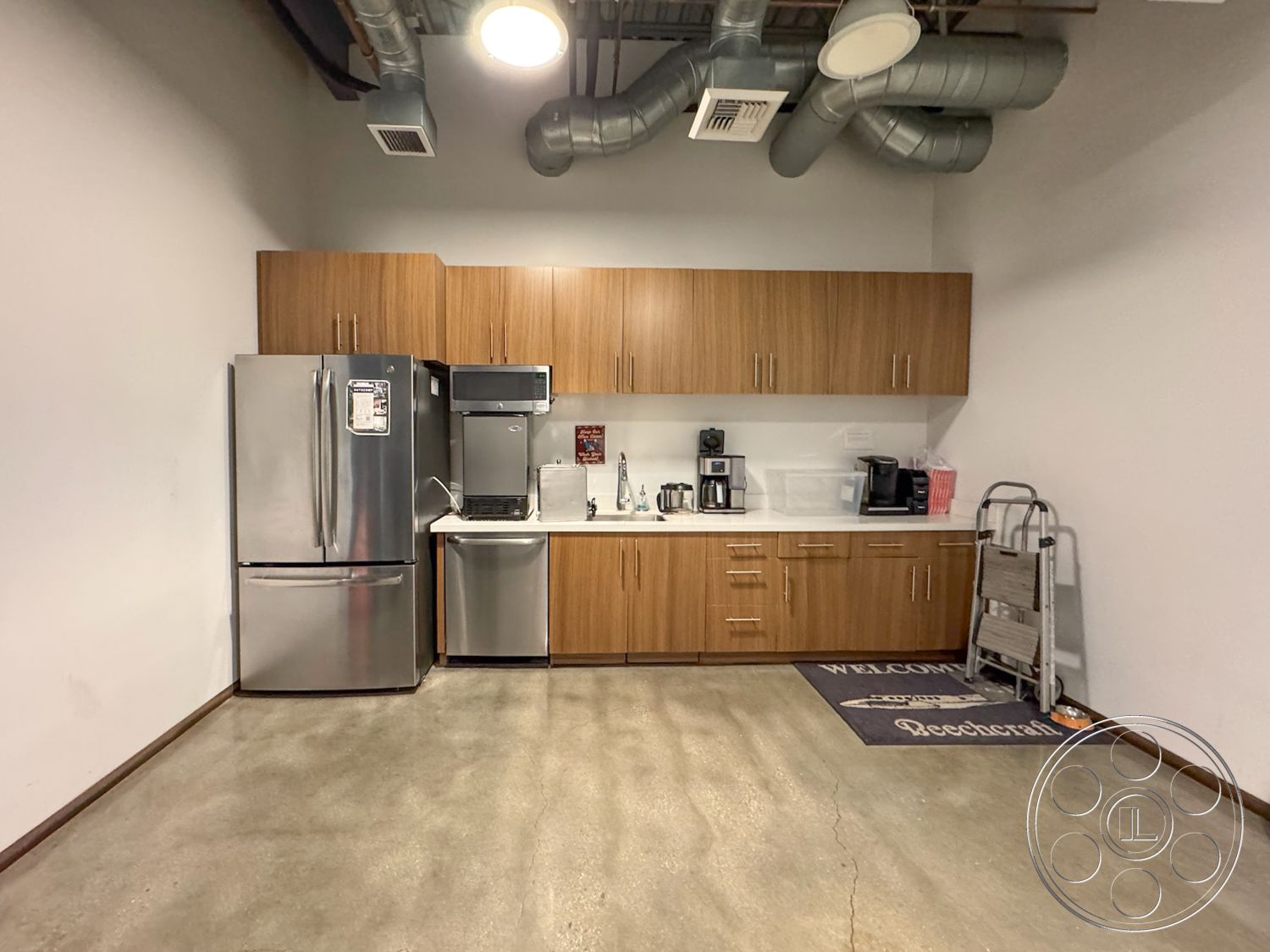 HW Hangar - stainless steel appliances, open shelving, concrete flooring, white marble countertop, interior kitchen space, minimalist design aesthetic, laminate wood kitchen cabinets, industrial ductwork ceiling, refrigerator installation, modern coffee station, grey accent rug, horizontal cabinet handles