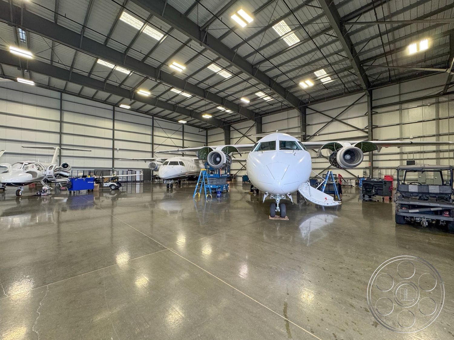 HW Hangar - exposed steel beams, open floor space, concrete polished floor, industrial style lighting, spacious interior layout, aircraft maintenance area, commercial aviation facility, maintenance workstations, hangar with natural light, aircraft service equipment, metal structure warehouse, steel frame hangar, high ceiling warehouse interior, large aircraft parking, motorized inspection lifts, equipment storage area, aviation workshop, mechanical service access, aircraft repair hangar