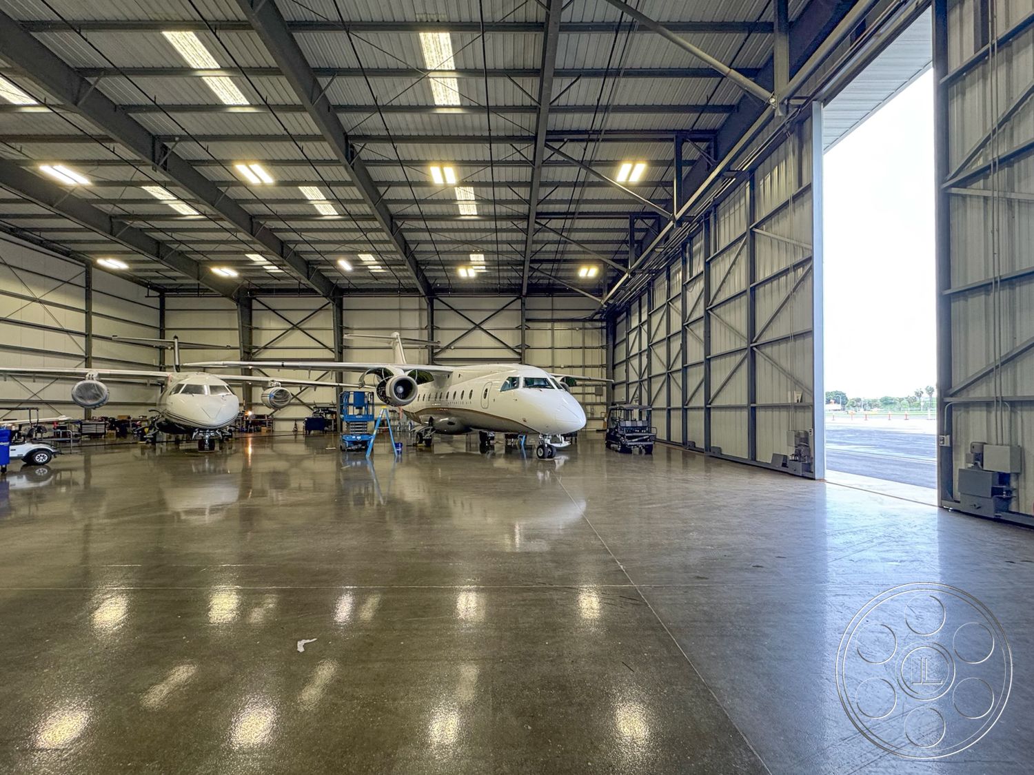 HW Hangar - workshop area, concrete polished floor, LED lighting fixtures, exposed steel structural elements, aircraft storage space, steel aircraft hangar interior, large bi-fold hangar doors, high vaulted ceiling with metal trusses, industrial space with maintenance area, floor-to-ceiling metal walls, aircraft maintenance workspace, wet cleaning area, open hangar layout, high bay space, tarmac view from hangar, service vehicle parking