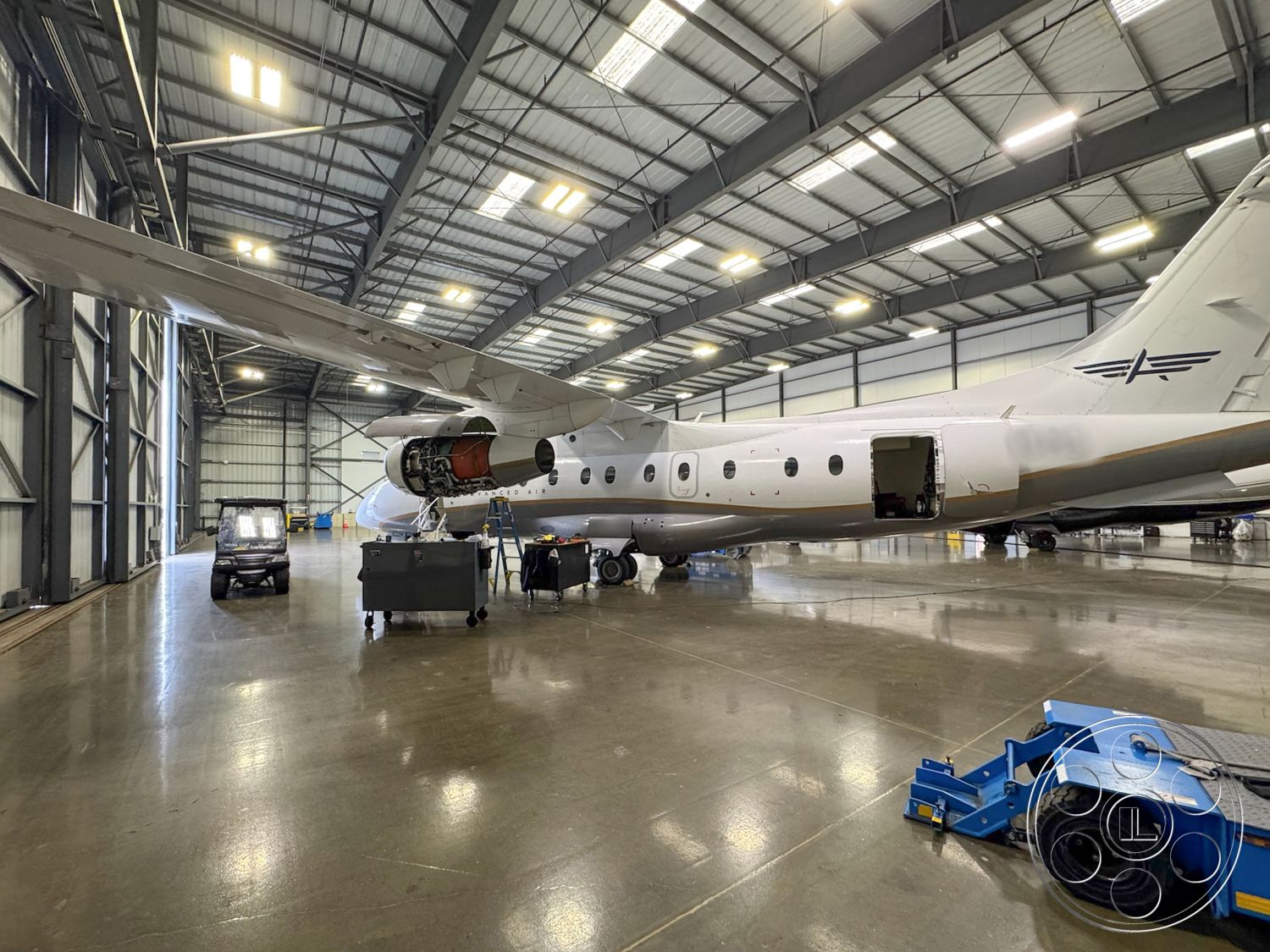 HW Hangar - industrial lighting fixtures, concrete polished floor, hangar door openings, aircraft maintenance area, metal aircraft hangar interior, heavy-duty equipment storage, aircraft service equipment, steel framing structure, high bay ceiling with skylights, large open space for aviation work, workshop area with tools, exposed ductwork features, maintenance workspace, non-slip surface flooring, metal tool cabinets, hanger interior with aircraft, spacious flight operation zone