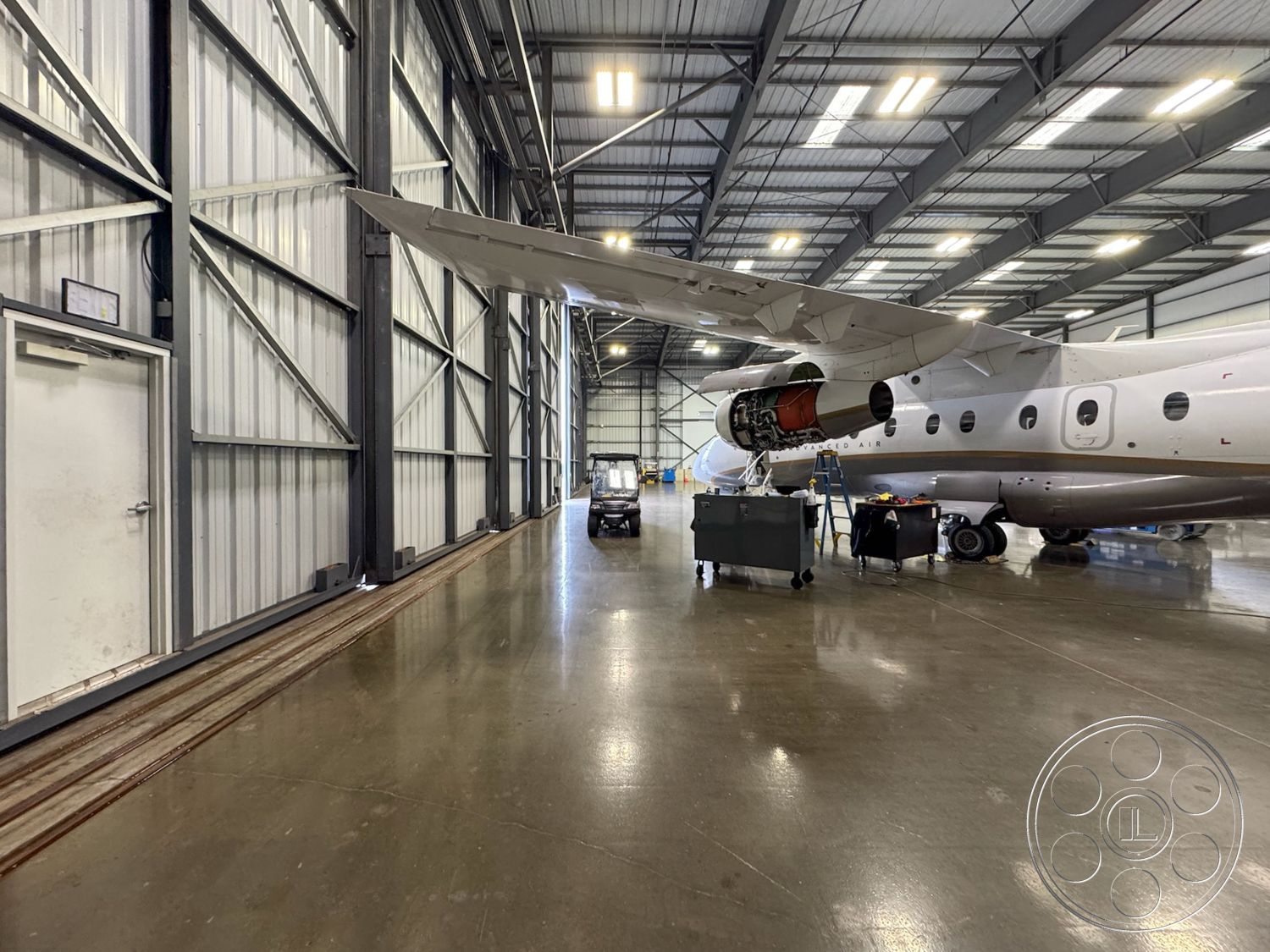 HW Hangar - concrete flooring, industrial lighting fixtures, corrugated metal walls, steel frame construction, clean lines and open layout, high ceiling with exposed beams, large sliding hangar doors, large aircraft maintenance area, equipment storage area, metal airplane hangar interior, open space for aircraft maintenance, hangar with ample natural light, marble polished concrete floor, maintenance tools and carts, airplane wing overhead