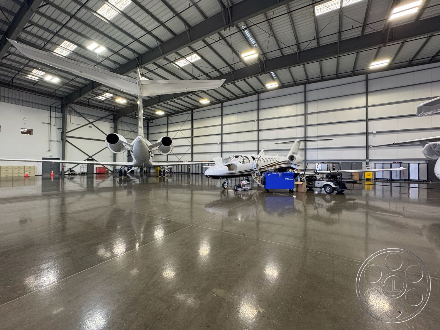 HW Hangar - exposed ductwork, modern industrial design, concrete slab foundation, aircraft maintenance area, concrete aircraft parking area, large sliding hangar doors, industrial ceiling with skylights, high-gloss epoxy flooring, clean and organized workspace, open floor plan hangar, metal truss structure, aero-dynamic hangar space, insulated steel wall panels, bright task lighting, commercial aviation hangar interior, metal beam framework, engine maintenance bays, aircraft service equipment area, hangar with large clearance, aviation storage solutions, safety signage and equipment, high ceilings with ventilation, strategically placed power outlets, accessible vehicle pathways