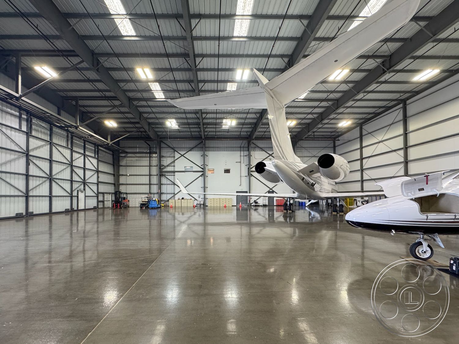 HW Hangar - concrete flooring, open space layout, industrial lighting fixtures, high vaulted ceiling, polished concrete surface, insulated wall panels, large hangar doors, exterior aircraft hangar, metal frame construction, equipment storage area, steel truss structure, hangar parking area for aircraft, engine maintenance area, maintenance shop, aircraft service entrance