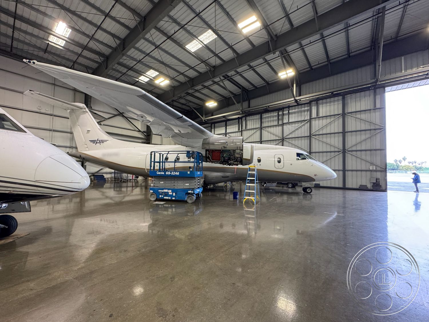 HW Hangar - industrial lighting fixtures, aircraft maintenance area, modern aviation facility, high ceiling with exposed metal beams, aircraft service area, steel aircraft hangar structure, concrete flooring with glossy finish, hangar door opening, mechanical workshop space, scissor lift for aircraft access, tarmac outside hangar, exterior hangar with large sliding doors, interior maintenance bay, reflective concrete surface, aviation tool storage area