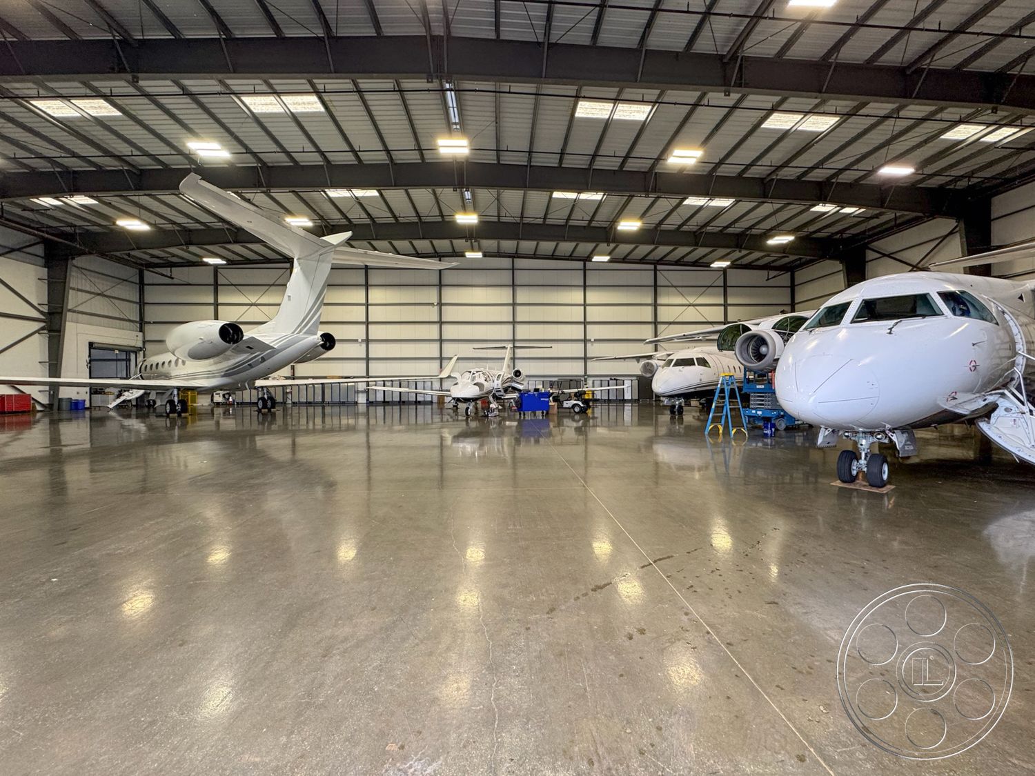 HW Hangar - open floor plan, concrete floor, utility area, functional workspace, industrial lighting fixtures, steel frame construction, exposed structural beams, polished concrete surface, metal roof structure, aircraft storage space, aviation maintenance area, hangar interior, large sliding hangar doors, high bay ceiling, aerodynamic airplane shapes, painted steel walls, drainage system flooring, commercial hangar space, wide open interior space, hangar environment