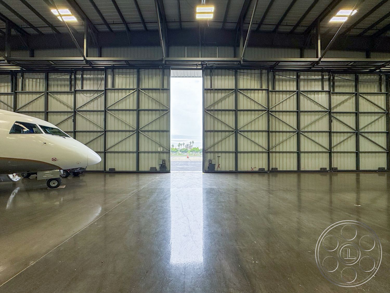 HW Hangar - concrete flooring, spacious interior, exposed structural elements, modern industrial design, industrial interior, neutral colored walls, aircraft storage space, open hangar space, hangar lighting fixtures, metal aircraft hangar structure, steel framed walls, glass overhead door, high ceiling beams, hangar with large entryway, contemporary hangar architecture, machinery space, airport environment