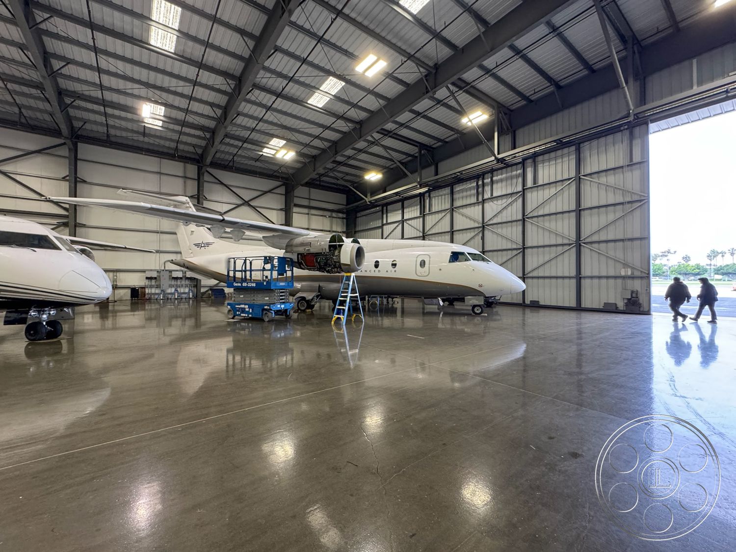 HW Hangar - industrial lighting fixtures, smooth concrete walls, concrete slab foundation, metal siding exterior, aircraft maintenance area, large hangar doors, interior hangar environment, exposed steel frame construction, metal roof support beams, high-gloss epoxy garage floor, rectangular hangar layout, ceiling-mounted ventilation system, open floor space for aircraft, service platform for aircraft