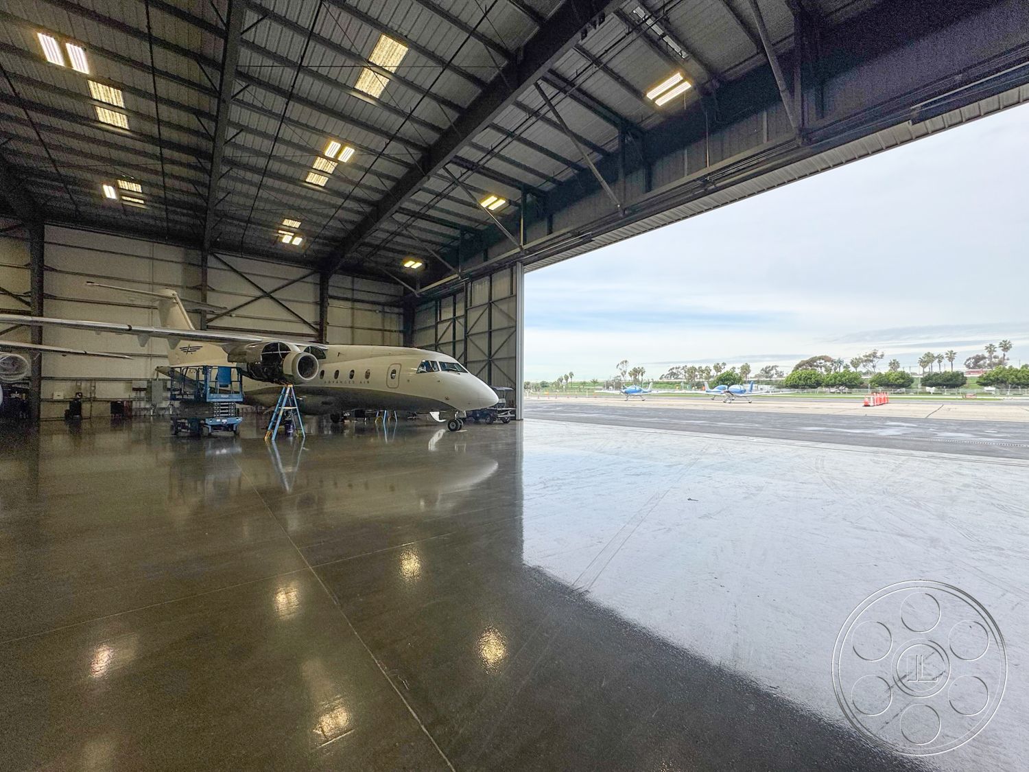 HW Hangar - high ceilings, open layout, concrete floor, spacious interior, industrial ceiling with exposed beams, aircraft maintenance area, large hangar doors, hangar lighting fixtures, steel hangar structure, commercial aviation environment, reflective polished concrete, aircraft storage, maintenance equipment area, fenced airport perimeter view, exterior with runway view