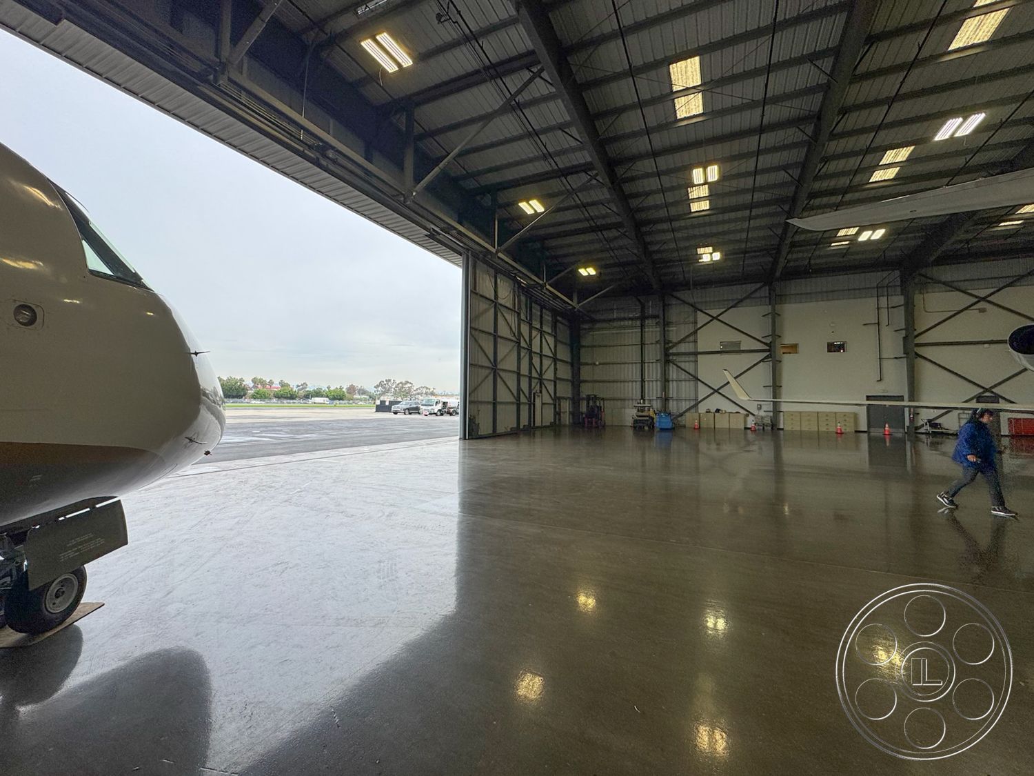 HW Hangar - polished concrete flooring, large glass windows, industrial lighting fixtures, aircraft parking area, interior airplane hangar, commercial aviation space, steel beam construction, wide-open space layout, exposed metal truss ceiling, large overhead door, maintenance equipment storage area, drainage system design, high ceiling clearance, reflective floor finish, safety cones for maintenance area