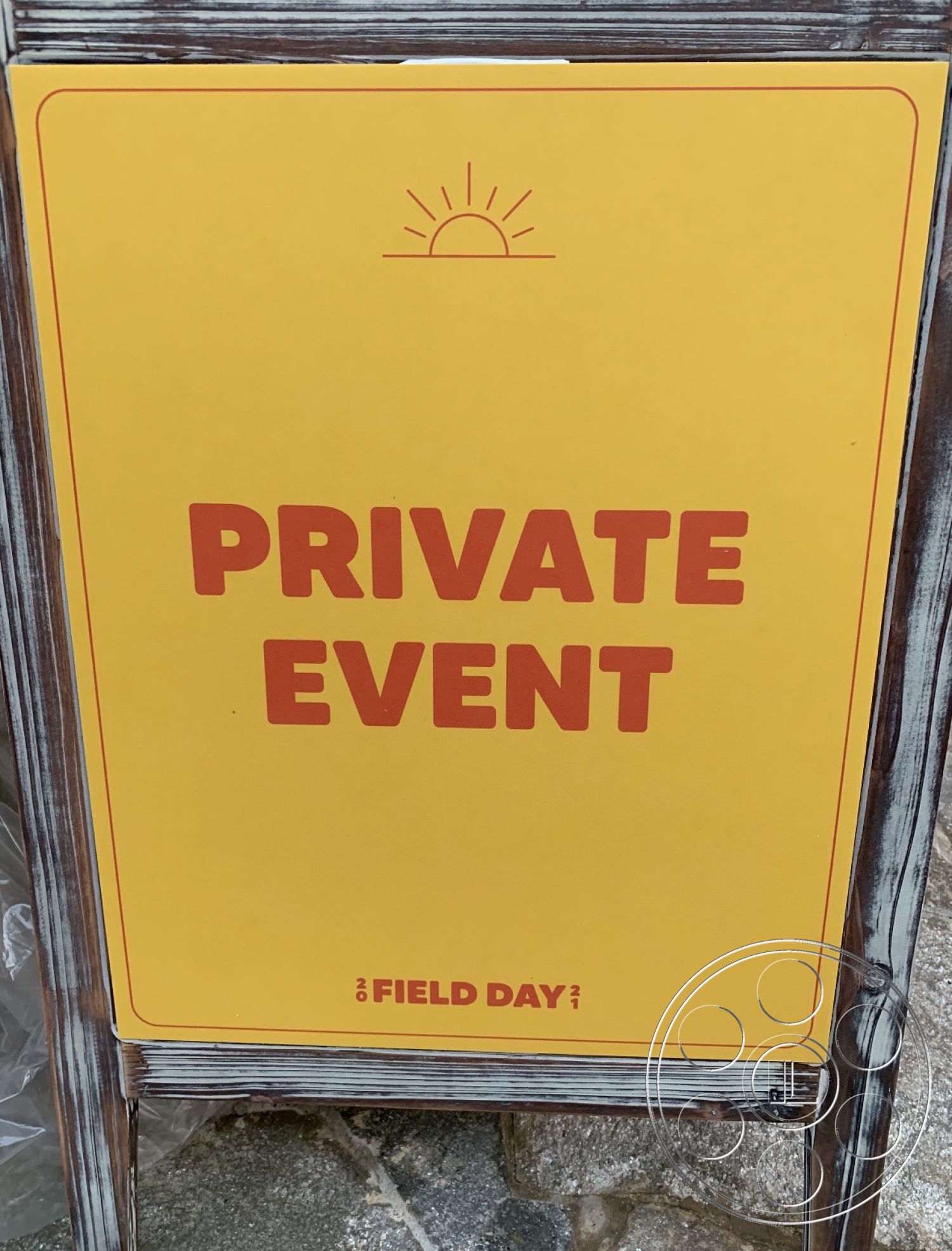 The Pink Beach House - wooden frame, exterior signboard, yellow printed sign, event notification, modern typography, sun emblem, private event signage, bold letter design, outdoor display, durable construction