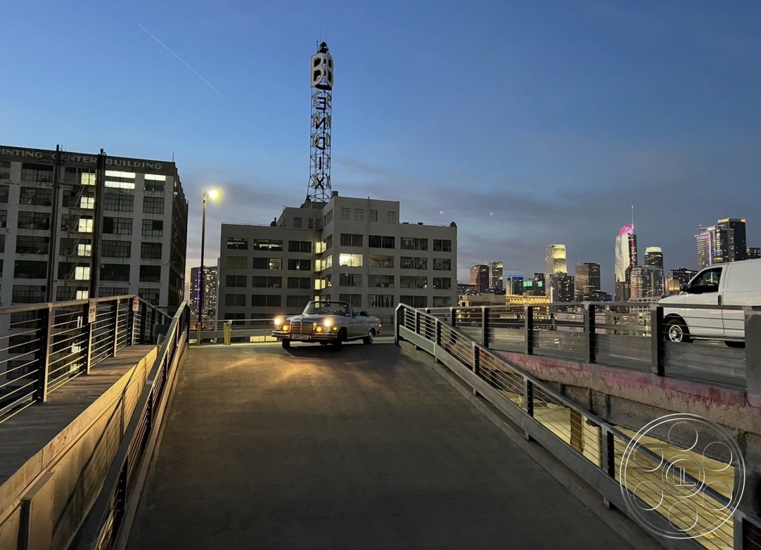 SKY Rooftop Garage - city skyline view, concrete parking surface, mixed-use urban environment, steel railing details, concrete support columns, exterior parking garage ramp, mid-century modern industrial architecture, urban rooftop parking area, historic brick building architecture, city lights at dusk, modern glass window facades, high-rise building surroundings, illuminated street lighting, open air deck space, vintage car parked