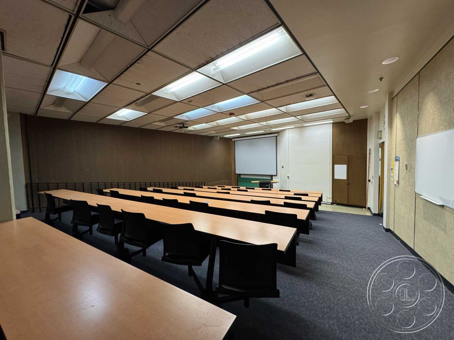 Old School - acoustic ceiling tiles, whiteboard wall, interior classroom space, projector screen wall, black plastic seating, drywall partition walls, wooden conference tables, carpet flooring in classroom, flourescent ceiling lighting, lecture hall seating arrangement, administrative office entrance, textured panel wall treatment
