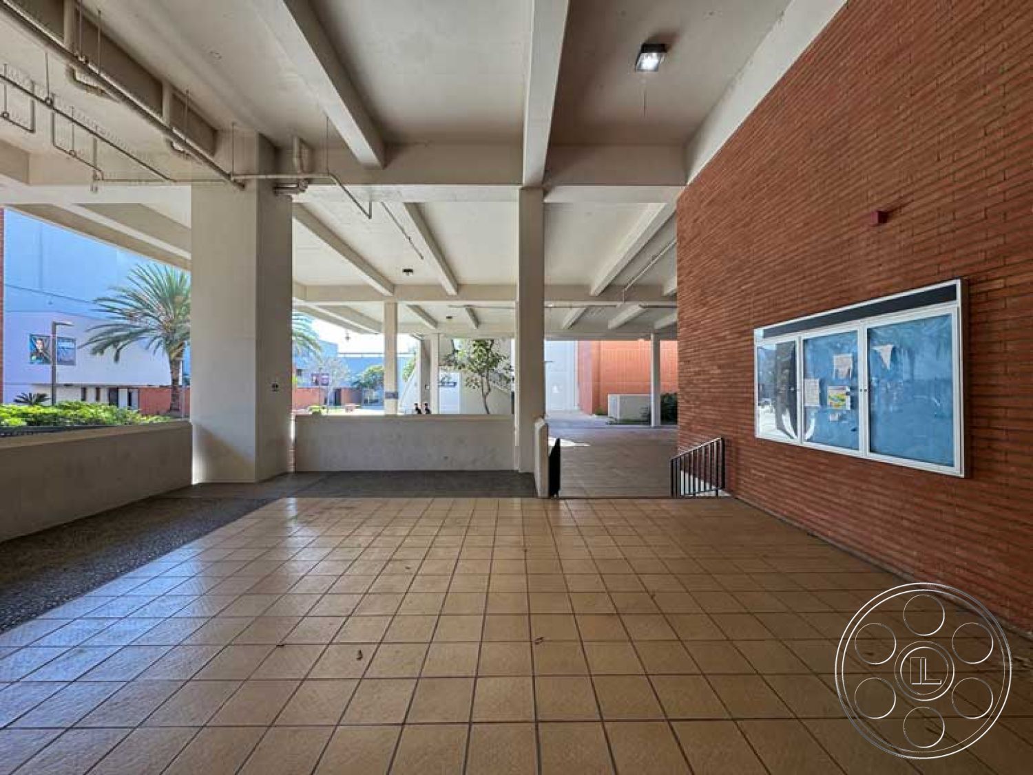 Old School - open space layout, modern design elements, exposed brick wall, landscaped garden area, palm tree landscaping, concrete support columns, urban architectural style, bright overhead lighting fixtures, exterior concrete tile flooring, open-air courtyard setting, tiled walkways, multi-level stairway with railing, textured brick wall