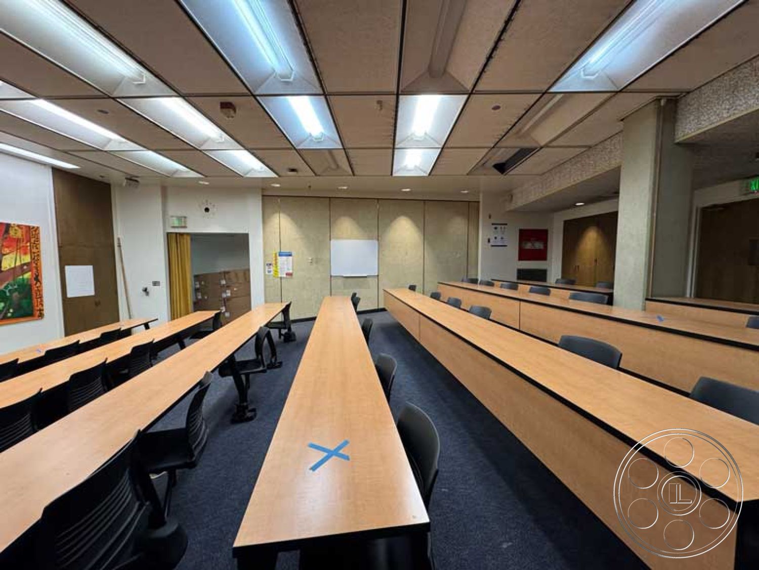 Old School - textured wall panels, light wooden cabinetry, acoustic ceiling tiles, fluorescent ceiling lights, interior classroom space, laminate classroom tables, carpeted classroom flooring, black plastic classroom chairs, dry erase board area, painted wall with artwork