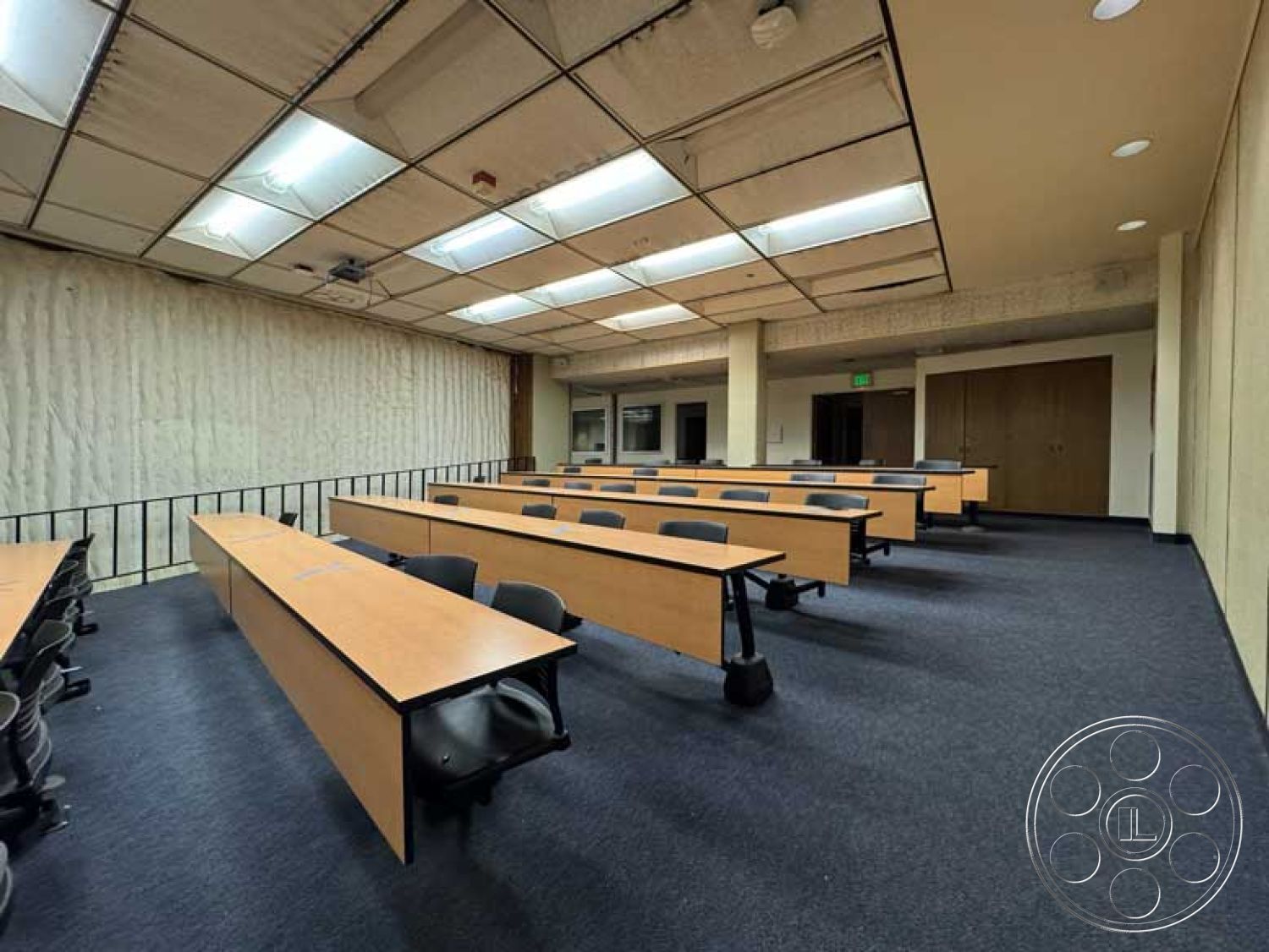 Old School - minimalist decor, textured wall panels, carpet flooring, black ergonomic chairs, acoustic paneling, large windows with natural light, drop ceiling with fluorescent lighting, interior classroom setting, wooden lecture tables, functional learning environment
