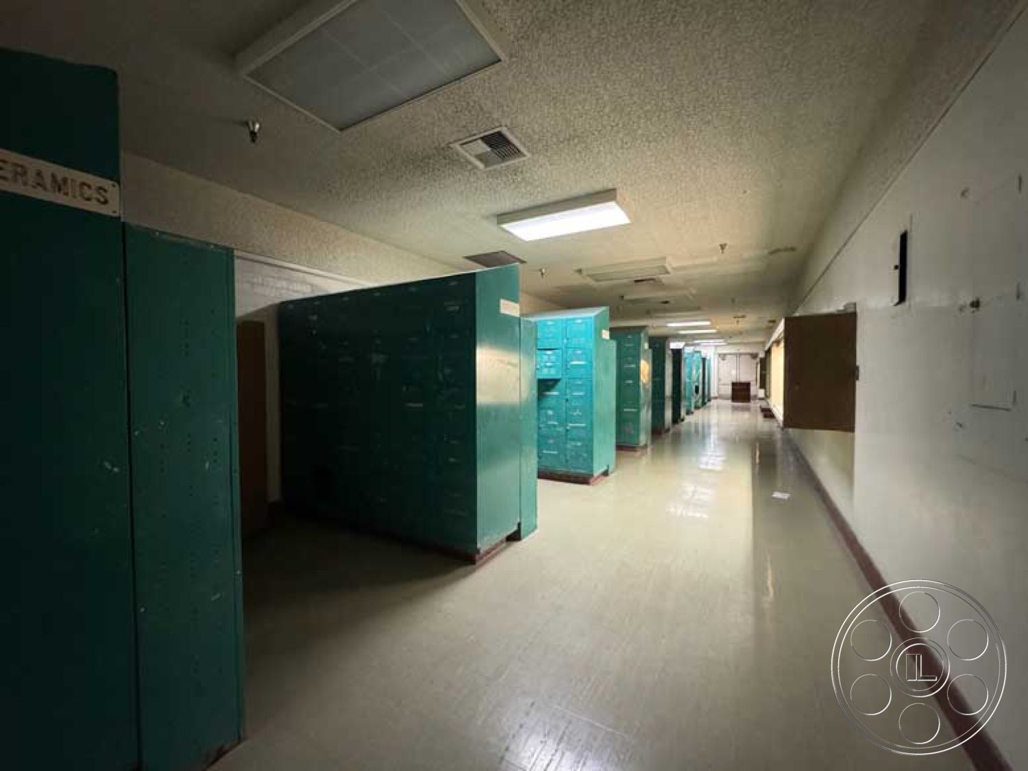 Old School - textured wall finish, laminate flooring, metal lockers, interior hallway, white painted walls, drop ceiling tiles, wood door frames, fluorescent ceiling lights, rectangular hallway layout, green metal locker banks, even lighting