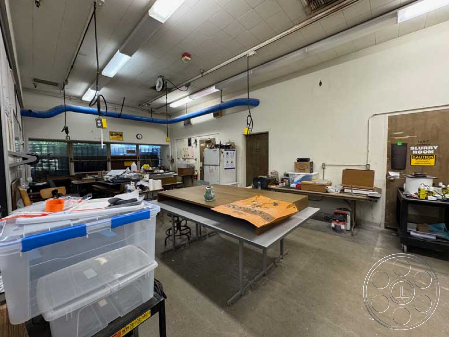 Old School - wooden cabinetry, large windows for natural light, functional workspace, multi-purpose area, exposed ductwork, storage boxes, painted drywall walls, open layout design, concrete floor finish, fluorescent lighting fixtures, interior workshop space, metal worktables, industrial ceiling with pipes, crafting area, collaboration zones, vertical wall-mounted storage, scooter for mobility, dry-erase boards for planning, suspended wires and cables, miscellaneous décor elements