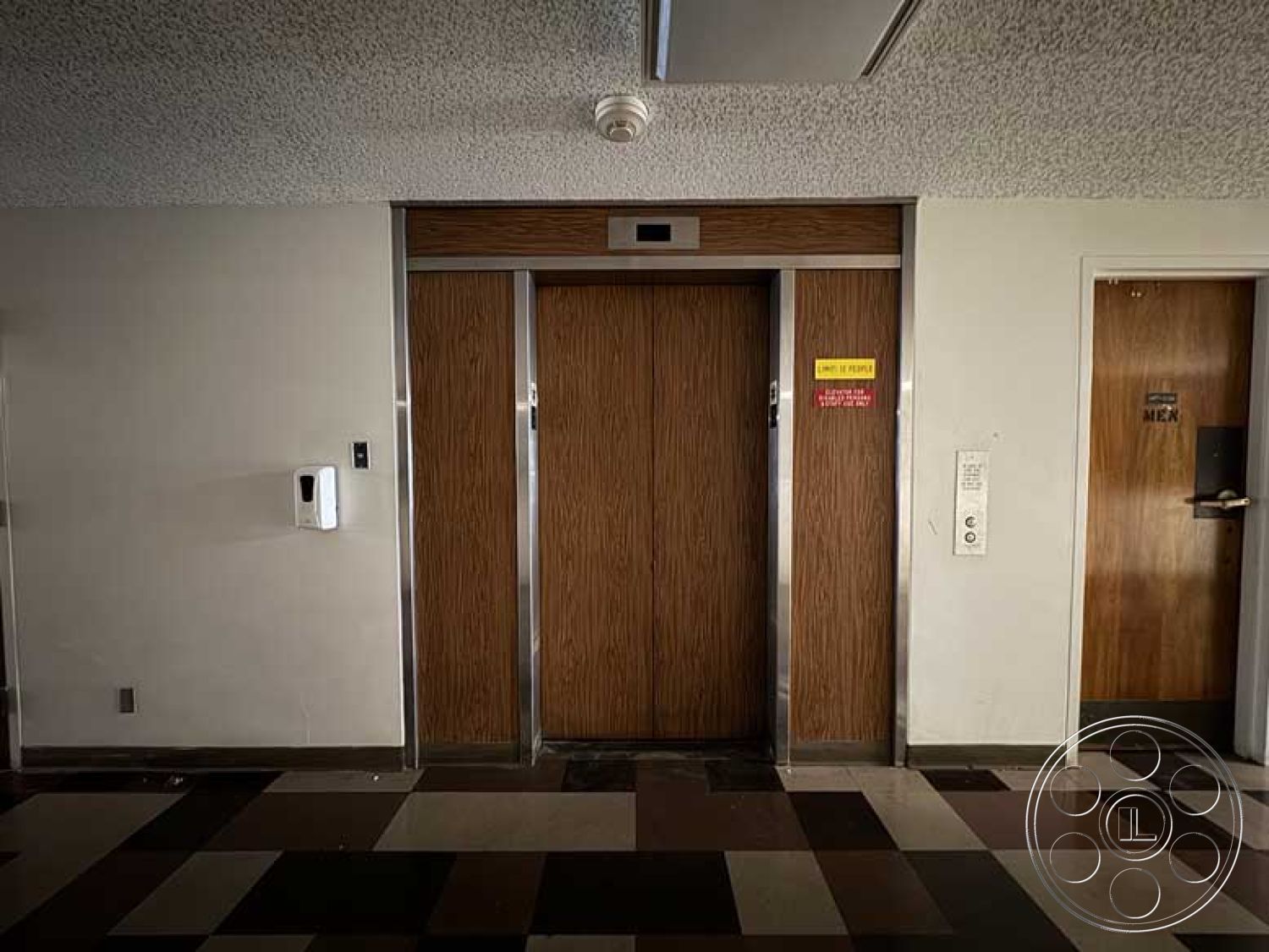 Old School - overhead fluorescent lighting, neutral wall paint, modern minimalist design, interior elevator lobby, textured ceiling tiles, traditional door style, wood panel elevator doors, elevator call button panel, chromed steel elevator frames, checkerboard floor tiles, brown and beige floor tiles, fire safety notice sign, nearby restroom door