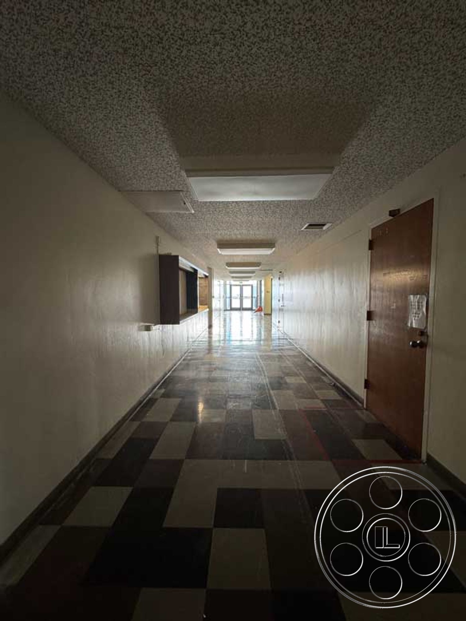 Old School - minimalist architectural style, commercial building interior, interior corridor space, plain painted walls, wooden entrance door, exposed acoustic ceiling tiles, tile flooring with checkered pattern, suspended fluorescent ceiling lights, open hallway with natural light, interior hallway lighting fixtures, modernistic corridor design, seamless transition from tiles to carpet, long straight hallway structure, built-in display area, direct access to exterior entrance