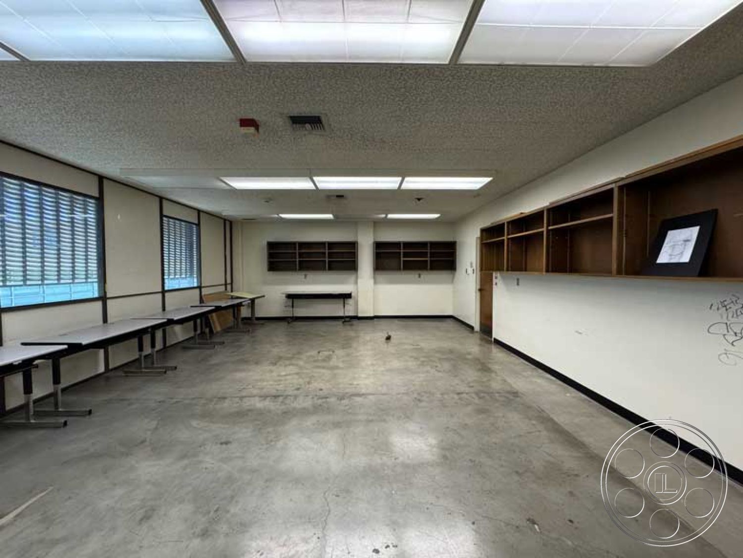 Old School - open layout, concrete floor, functional workspace, modular furniture, exposed ceiling, double-glazed windows, drop ceiling panels, flush-mounted ceiling lights, interior classroom setting, natural light source, plywood wall shelves, industrial-style room, neutral-colored walls