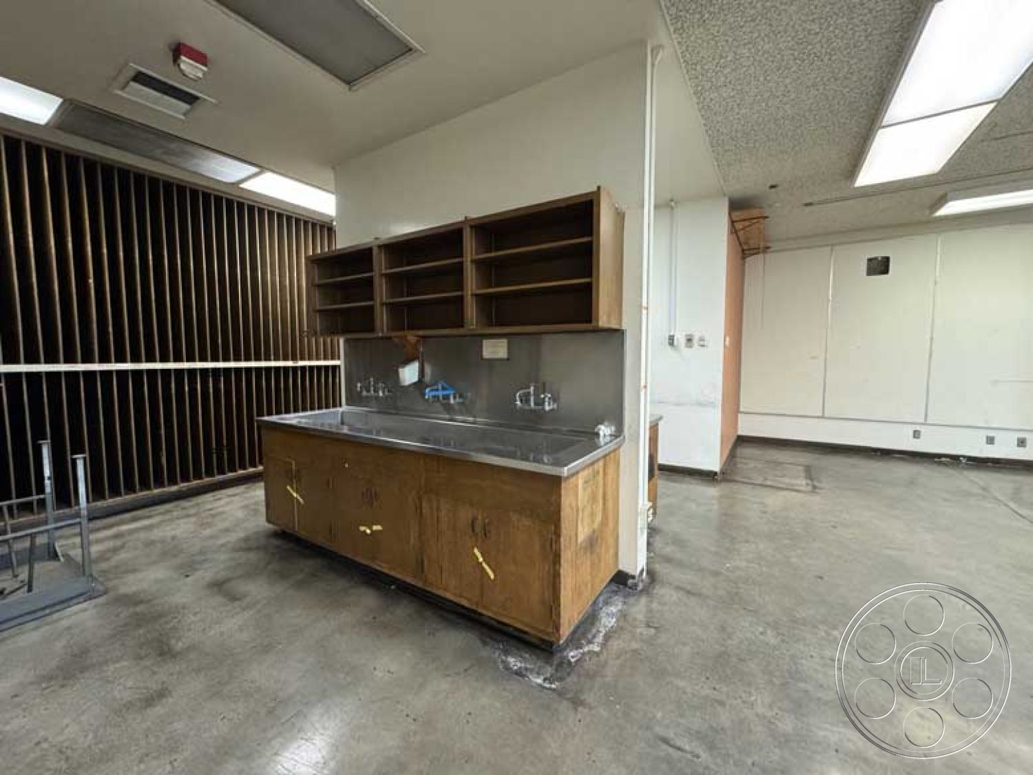 Old School - neutral color palette, minimalist aesthetic, open floor plan, wooden cabinetry, industrial design, exposed concrete floor, recessed ceiling lights, modern shelving units, stainless steel countertop, horizontal wood slat wall, commercial kitchen space, corner plumbing fixtures, unfinished wall surfaces, integrated electrical outlets