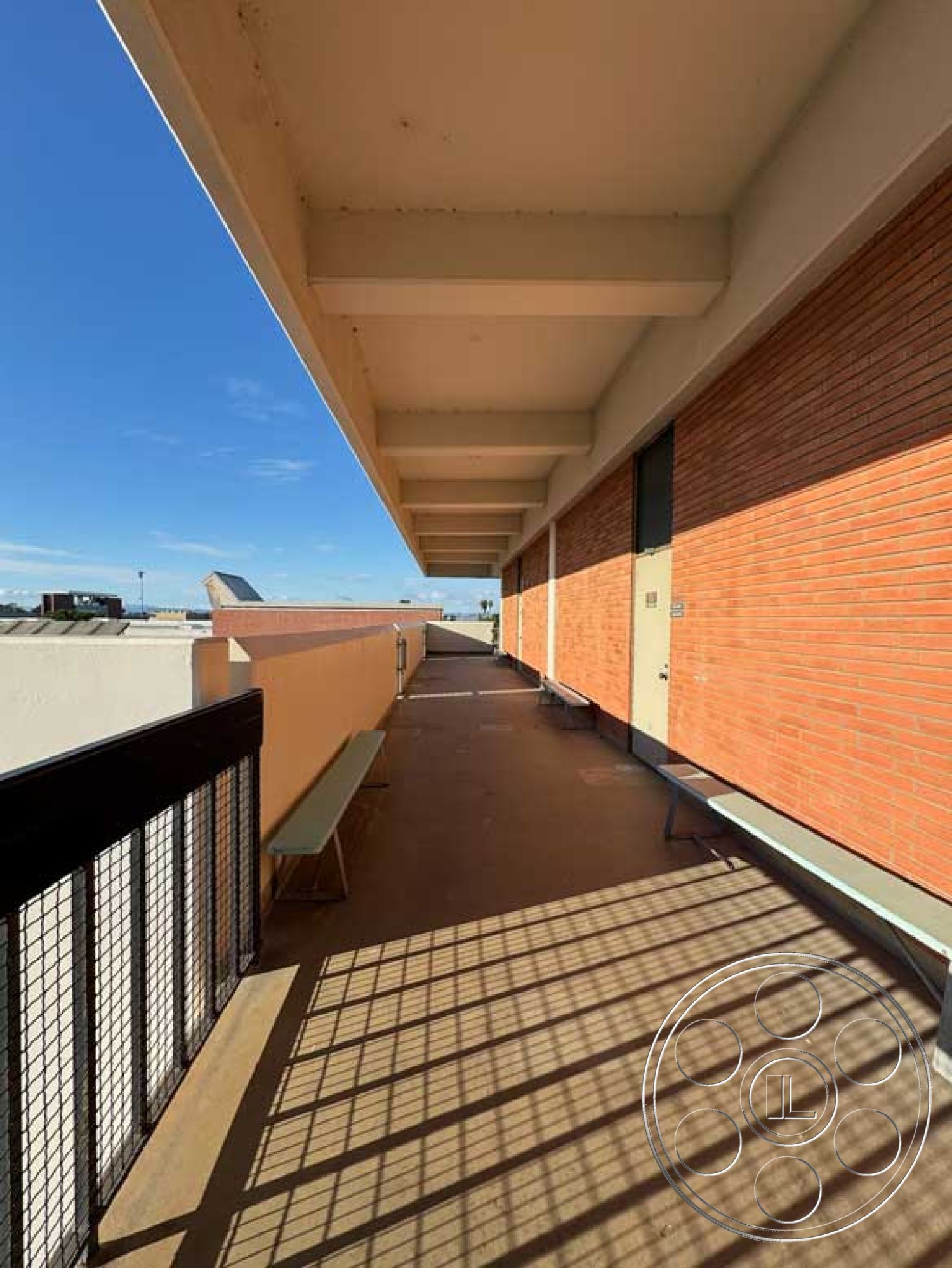 Old School - large glass windows, outdoor seating area, smooth concrete flooring, industrial design elements, minimalist architectural style, open sky view, urban rooftop setting, exterior balcony area, reinforced concrete ceiling beams, red brick wall cladding, metal railing with grid pattern, sundrenched walkway
