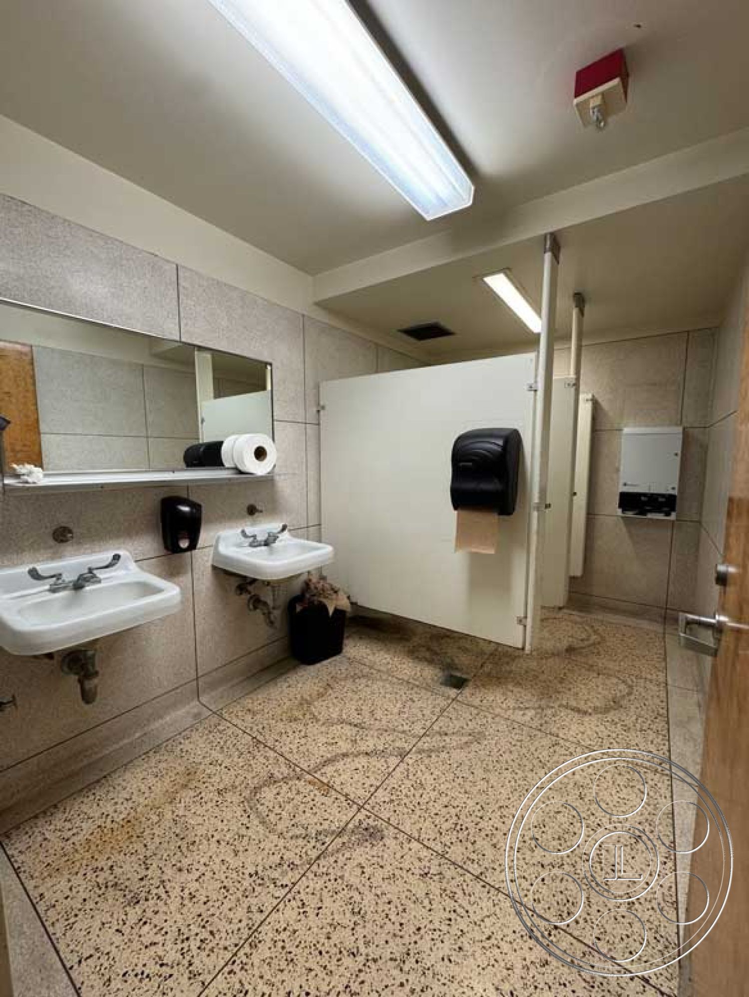 Old School - terrazzo bathroom flooring, interior restroom design, exposed fluorescent ceiling lights, concrete bathroom walls, chrome sink faucets, dual pedestal sinks, standard bathroom mirrors, translucent acrylic partitions, metal soap dispenser, plain paper towel dispenser, tile accent near mirrors, flush restroom stall doors, commercial bathroom layout