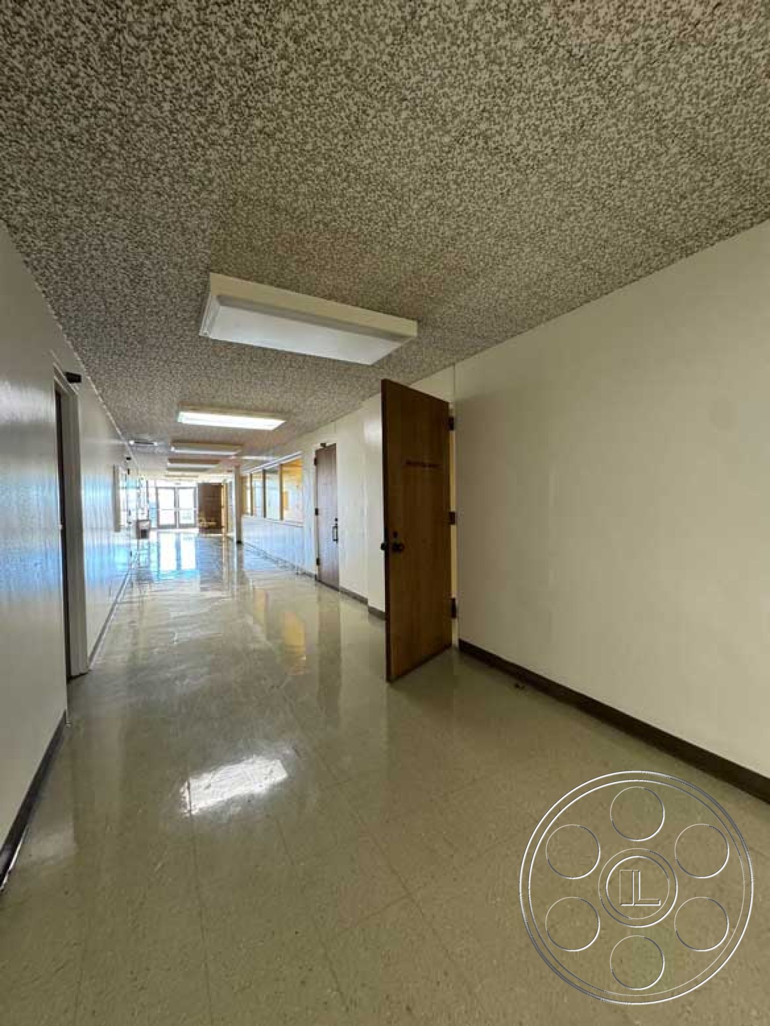 Old School - acoustic ceiling tiles, interior hallway, white painted walls, minimalist architectural design, large windows with natural light, fluorescent ceiling lights, wooden door frames, double wooden doors, glossy vinyl flooring, linear corridor layout