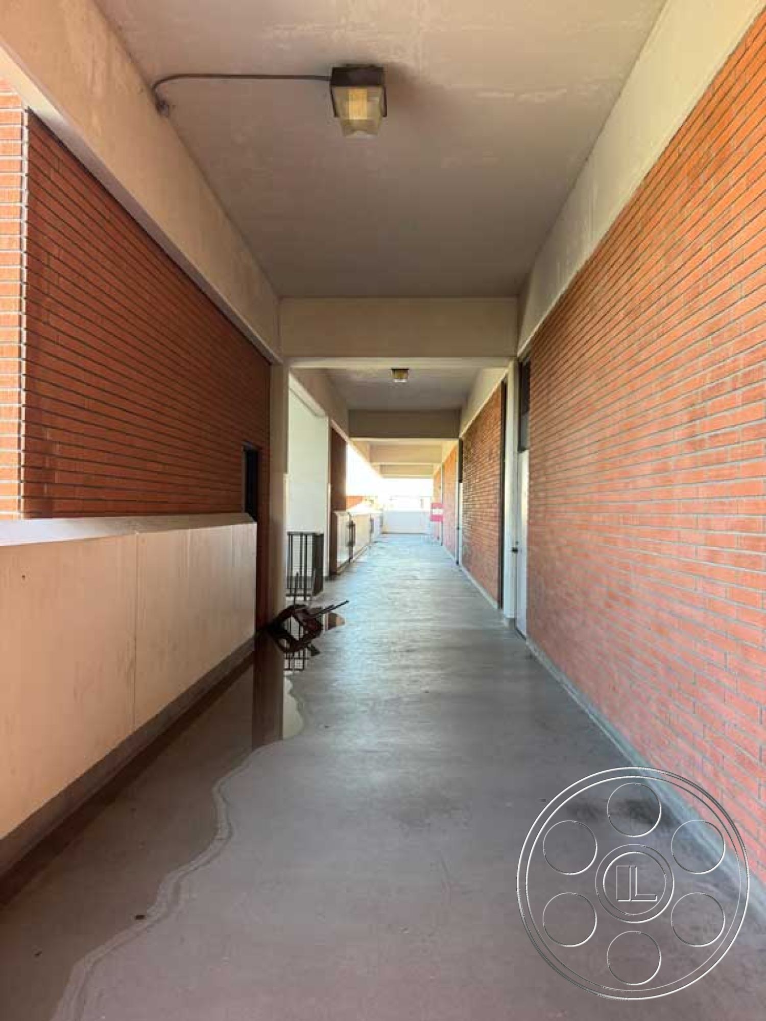 Old School - industrial architectural style, exposed brick corridor walls, concrete walkway floor, flat ceiling with integrated lighting, horizontal window openings, minimalist exterior lighting fixtures, smooth plaster ceiling finish, long linear hallway layout, secured entry features, reinforced concrete structure, urban setting corridor, interior passageway design