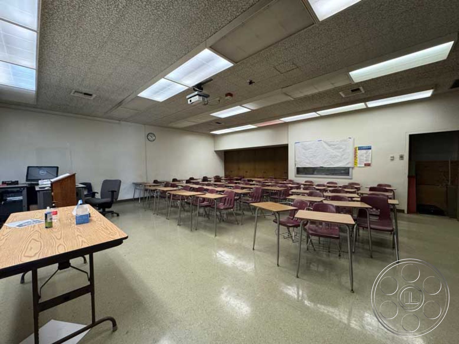 Old School - concrete block walls, chalkboard wall, metal folding chairs, educational environment, white painted walls, drop ceiling tiles, fluorescent ceiling lights, vinyl tile flooring, interior classroom space, glass window with blinds, open classroom layout, wooden teacher's desk, cork bulletin board, electronic projector mounted, large classroom windows, academic setting, school classroom design