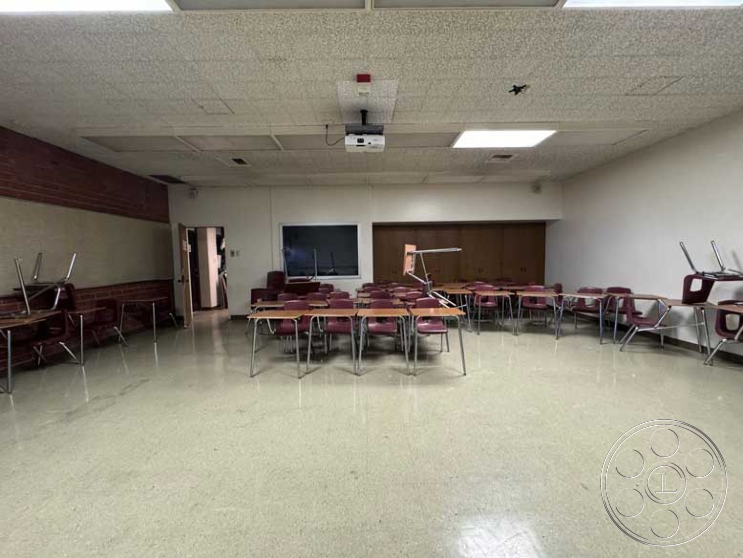 Old School - multi-functional space, brick accent wall, vinyl flooring, educational environment, neutral painted walls, built-in storage cabinets, acoustic tile ceiling, interior classroom space, organized classroom layout, overhead projector setup, foldable metal chairs, rectangular tables, light source from ceiling lights
