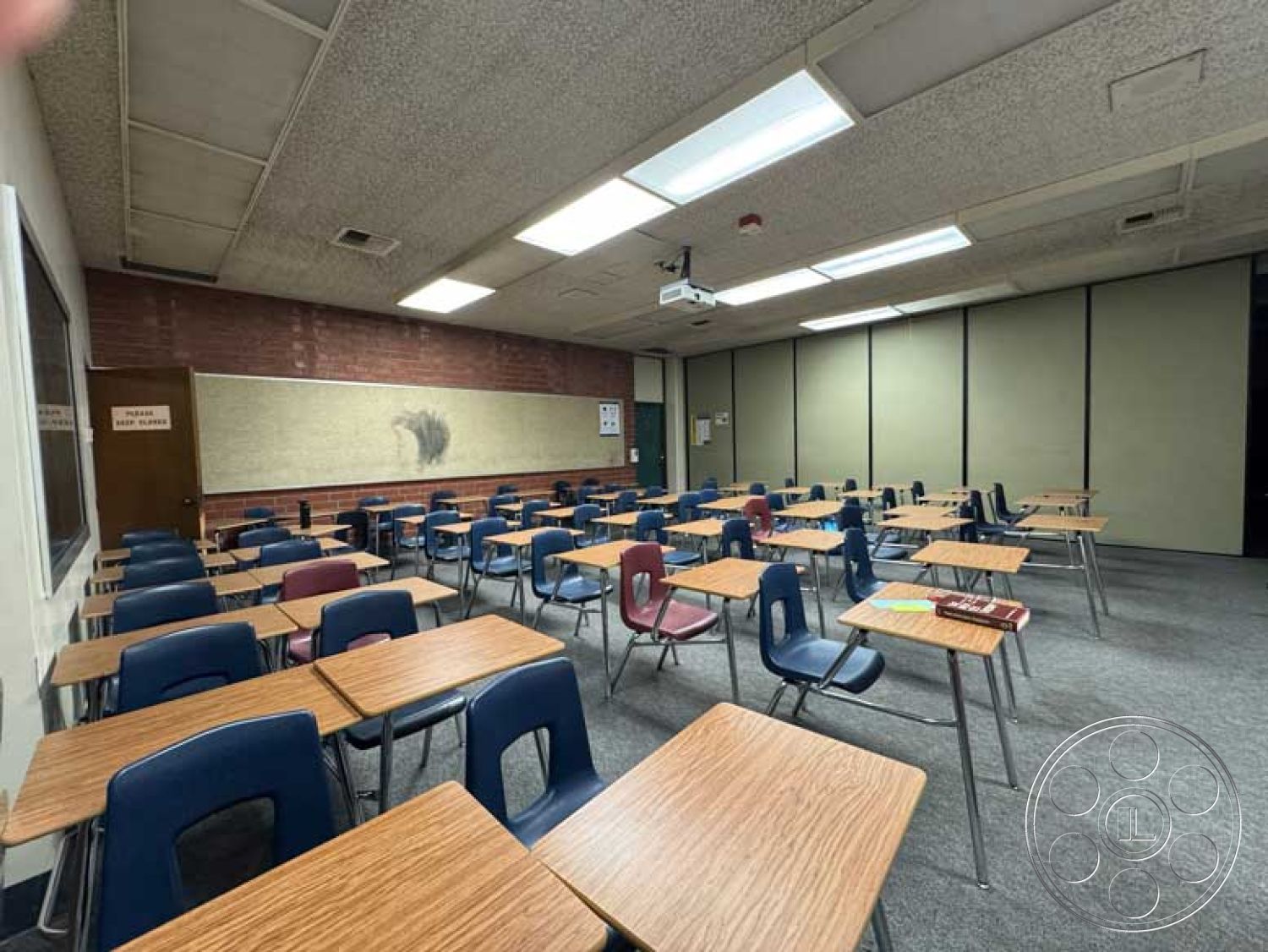 Old School - grey carpet flooring, educational setting, exposed brick accent wall, acoustic tile ceiling, dark wood paneling accents, rectangular classroom layout, metal-framed chairs, laminate classroom desks, projector mounting system, interior classroom environment, community school classroom, traditional teaching space