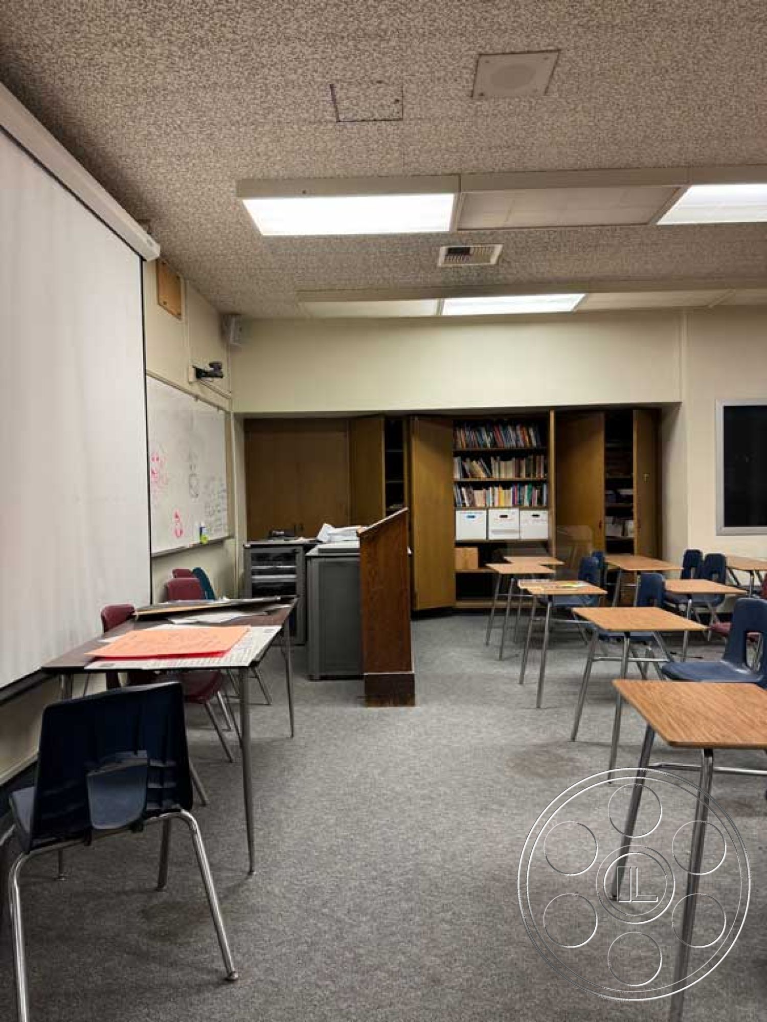 Old School - educational environment, white painted walls, functional space design, wall-mounted whiteboard, classroom setting, carpet flooring in classroom, metal frame student desks, exterior classroom design, wooden teacher's podium, suspended ceiling with fluorescent lights, open shelving for classroom resources, fabric-upholstered chairs, textbook storage cabinet, grouped seating arrangement