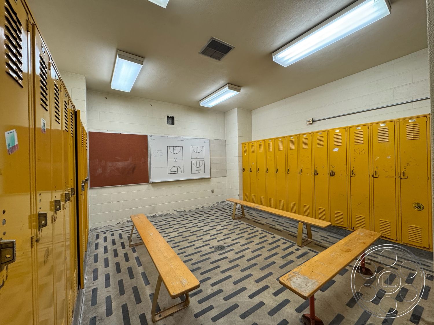 Old School - concrete block walls, wooden bench seating, fluorescent ceiling lights, striped vinyl flooring, interior locker room, open ceiling design, yellow metal lockers, rubber flooring with textured pattern, chalkboard wall for sports drawings, functional space for team changing