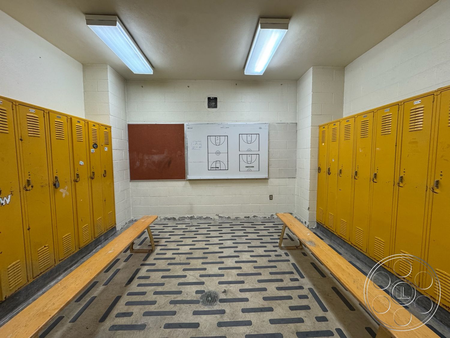 Old School - concrete block walls, fluorescent ceiling lights, industrial style space, interior locker room, yellow metal locker units, laminate wooden benches, rubber flooring with drainage patterns, chalkboard wall for basketball strategy, dry erase board for team discussions, functional athletic environment