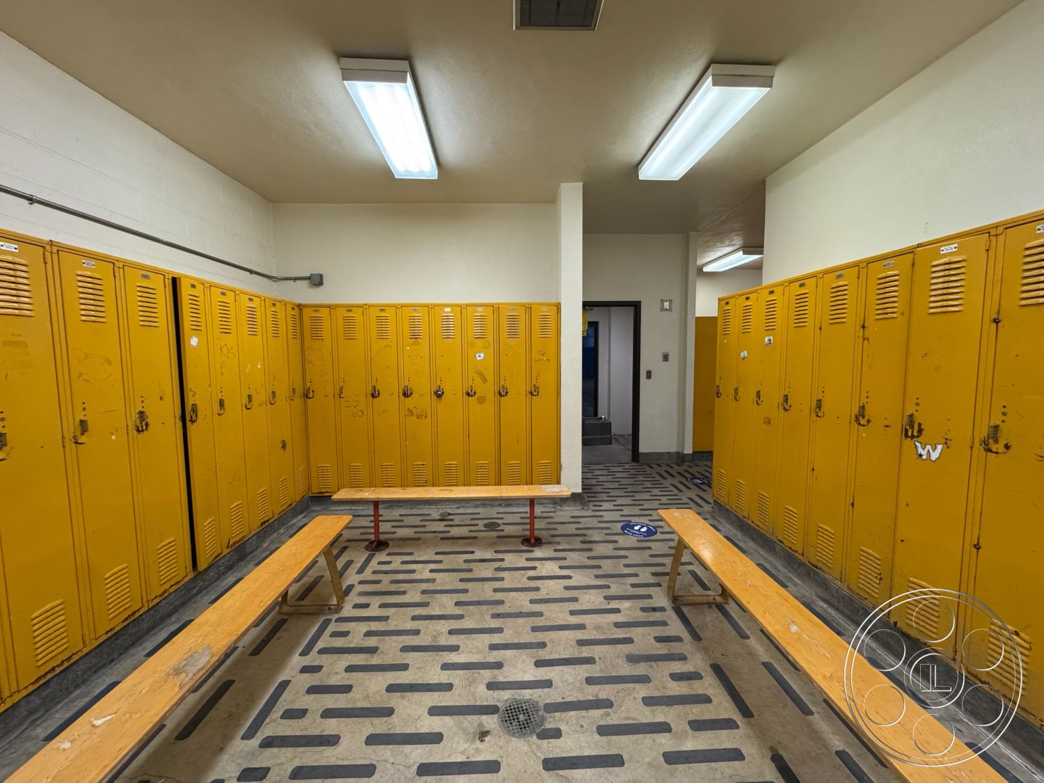 Old School - concrete walls, utilitarian design, fluorescent lighting fixtures, interior locker room, metal lockers with yellow finish, wood benches with natural finish, vinyl flooring with textured pattern, open layout changing area, functional athletic space, school locker facility
