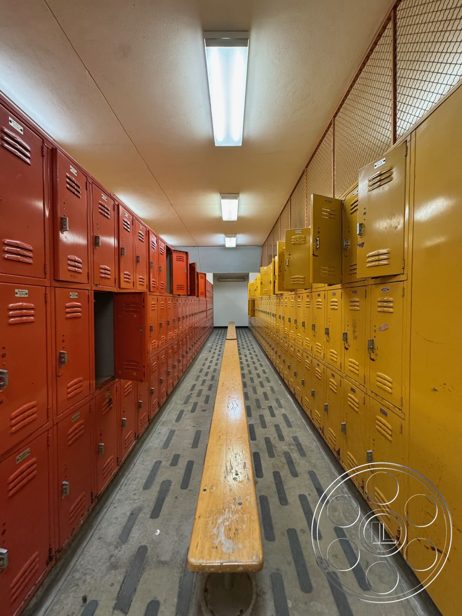 Old School - concrete flooring, high ceiling, ventilation system, metal lockers, wood bench seating, fluorescent ceiling lights, interior locker room, wire mesh partitions, yellow metal lockers, striped rubber flooring, orange metal lockers, angled corridor layout, functional minimalist design