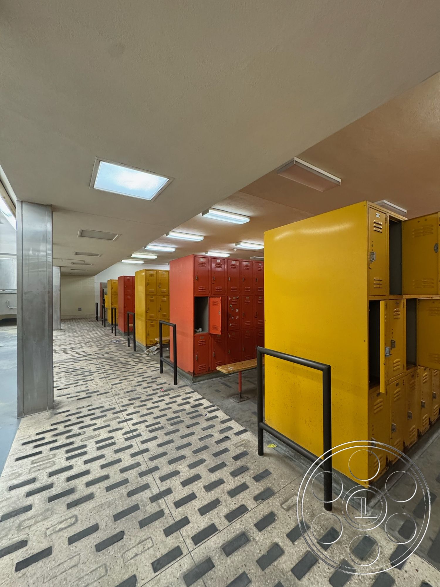 Old School - spacious layout, fluorescent ceiling lights, interior locker room, metal lockers in bright colors, yellow and red metal lockers, plastic laminate bench, concrete floor with textured finish, composite ceiling tiles, steel railing partitions, commercial locker facility, public restroom area, utility space with functional design, industrial locker setup