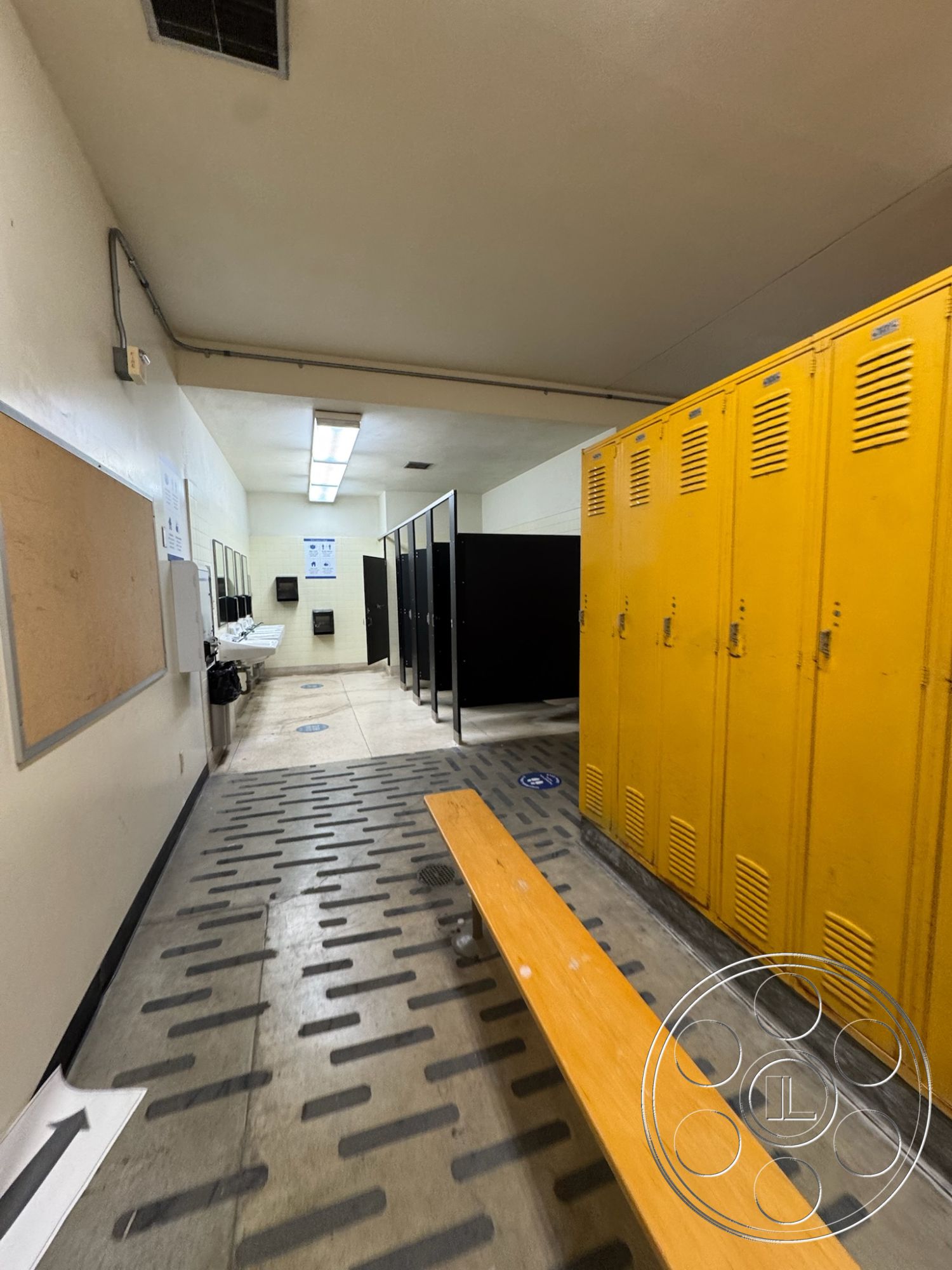 Old School - spacious layout, exposed ceiling, wooden bench seating, fluorescent ceiling lights, plywood wall panels, industrial locker room design, interior locker room, athletic facility interior, yellow metal lockers, black partition stalls, concrete flooring with textured finish, wet area drainage, tile accents near lockers, high-traffic flooring, male changing area, functional locker space, community recreation center, locker room amenities, sanitary environment features, sports facility locker space