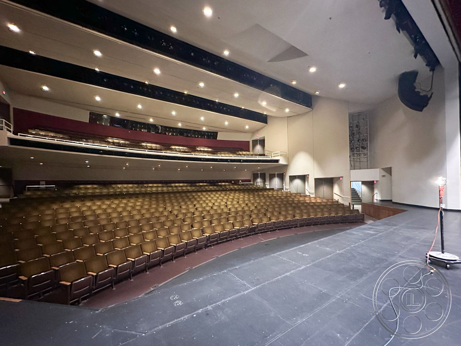 JT Theatre - neutral wall colors, backstage access, recessed lighting fixtures, black stage flooring, acoustic panel ceiling, modern theater architecture, interior theater design, emergency exit signage, multi-tiered seating arrangement, auditorium seating layout, curved theater seating, wall-mounted sound equipment, open auditorium space, accessibility ramps, stage with proscenium arch