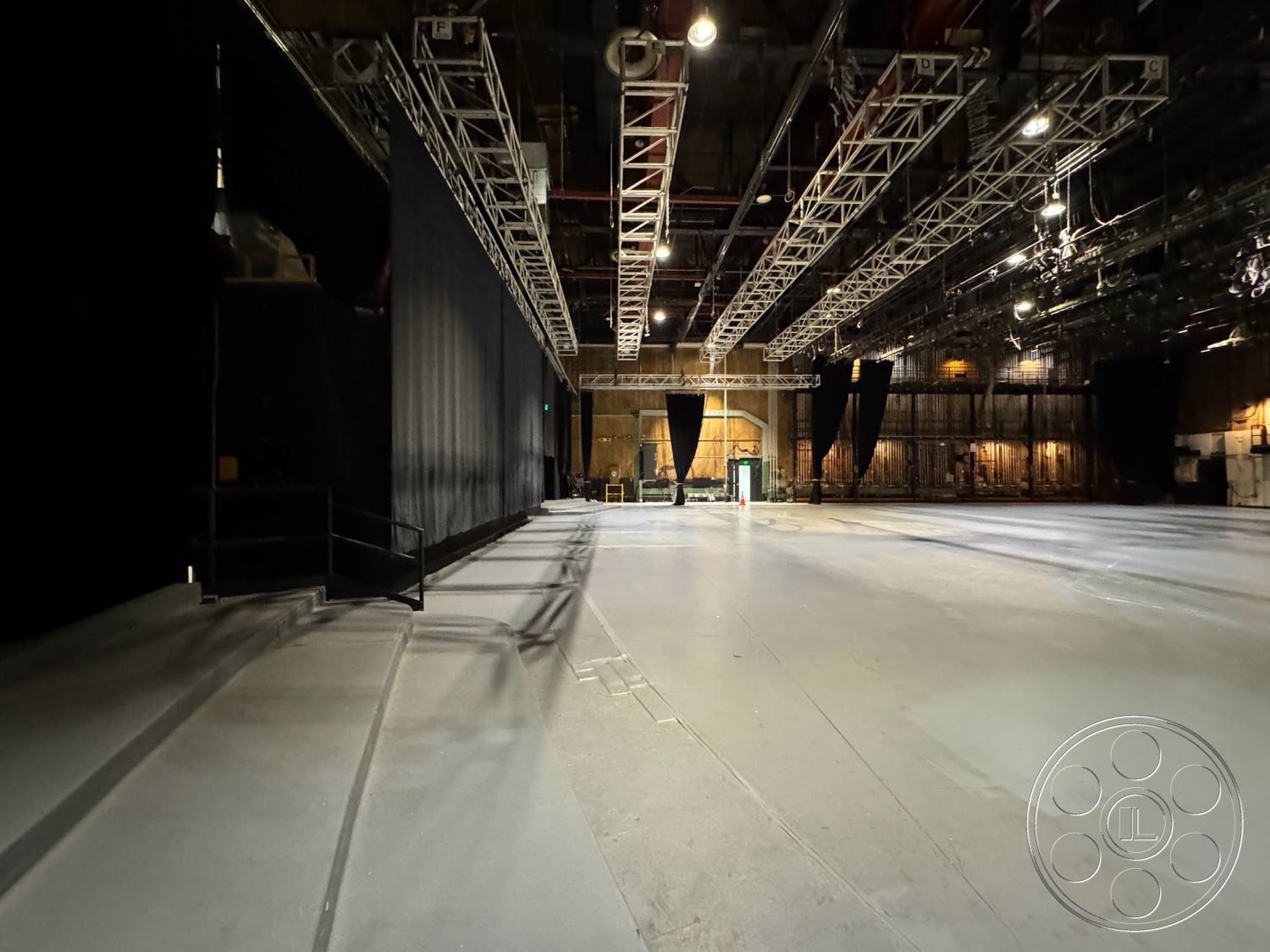 Stage 33 - high ceilings, neutral color palette, open floor plan, multifunctional space, textured concrete walls, industrial lighting fixtures, exposed steel beams, flexible performance area, concrete studio floor, black curtain wall, metal truss framework, soundproof studio environment, wide entryway, raw finishing details, production studio interior