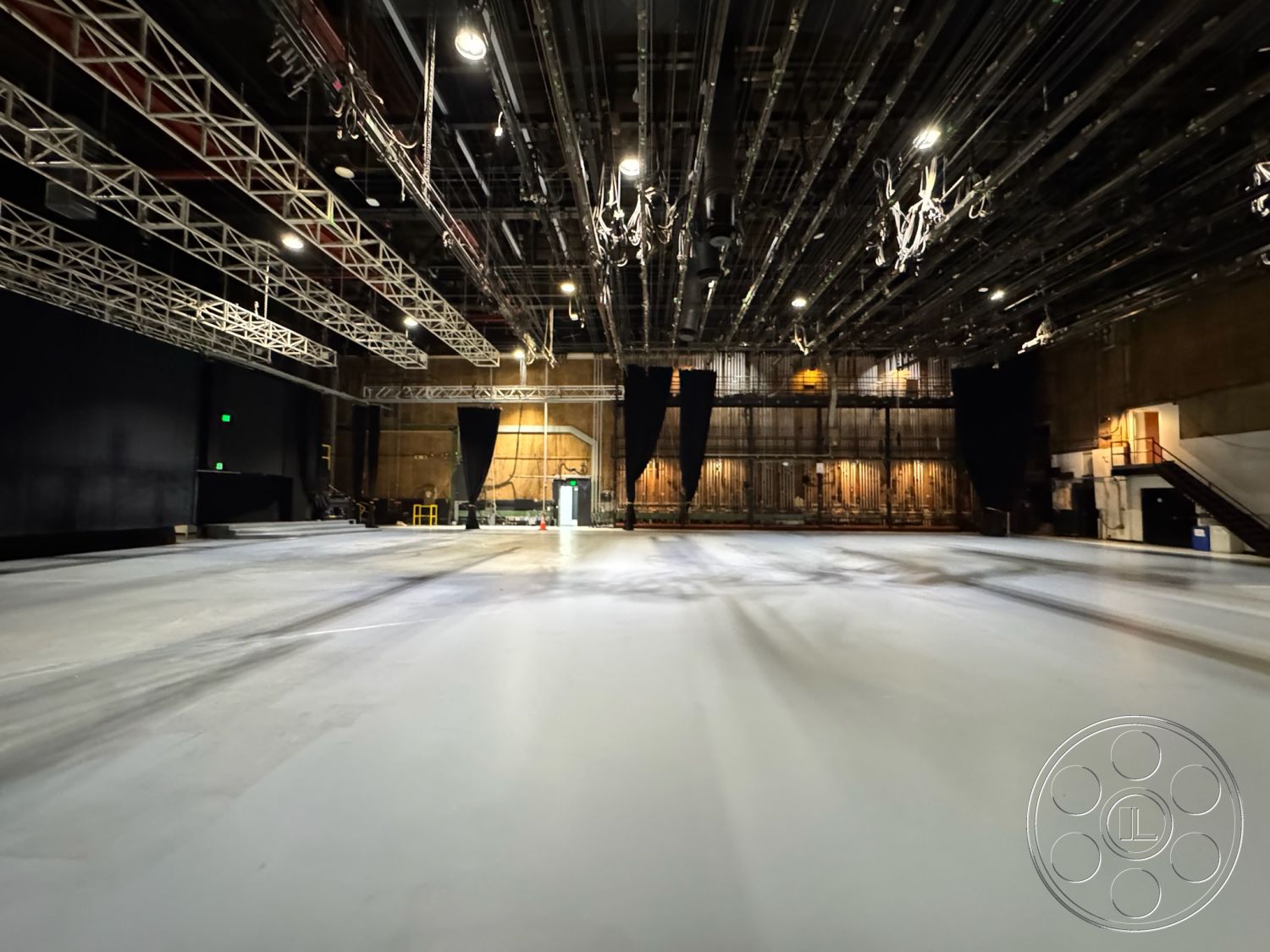 Stage 33 - interior space, wooden wall panels, backstage access, studio environment, acoustic paneling, industrial stage lighting, utility access points, smooth polished concrete floor, high ceiling with rigging, exposed overhead truss framework, black theatrical curtains, dimmer light fixtures, large open performance space, whitewashed brick walls, versatile performance area, flexible staging layout