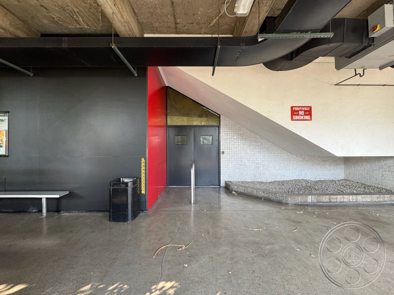 Stage 33 - urban setting, red accent wall, exposed concrete ceiling, commercial interior, black painted walls, textured tile wall treatment, minimalist interior, industrial-style lighting, glass entry doors, metal bench seating, grey polished concrete floor, asymmetrical architectural design, outdoor gravel landscaping, no smoking sign detail