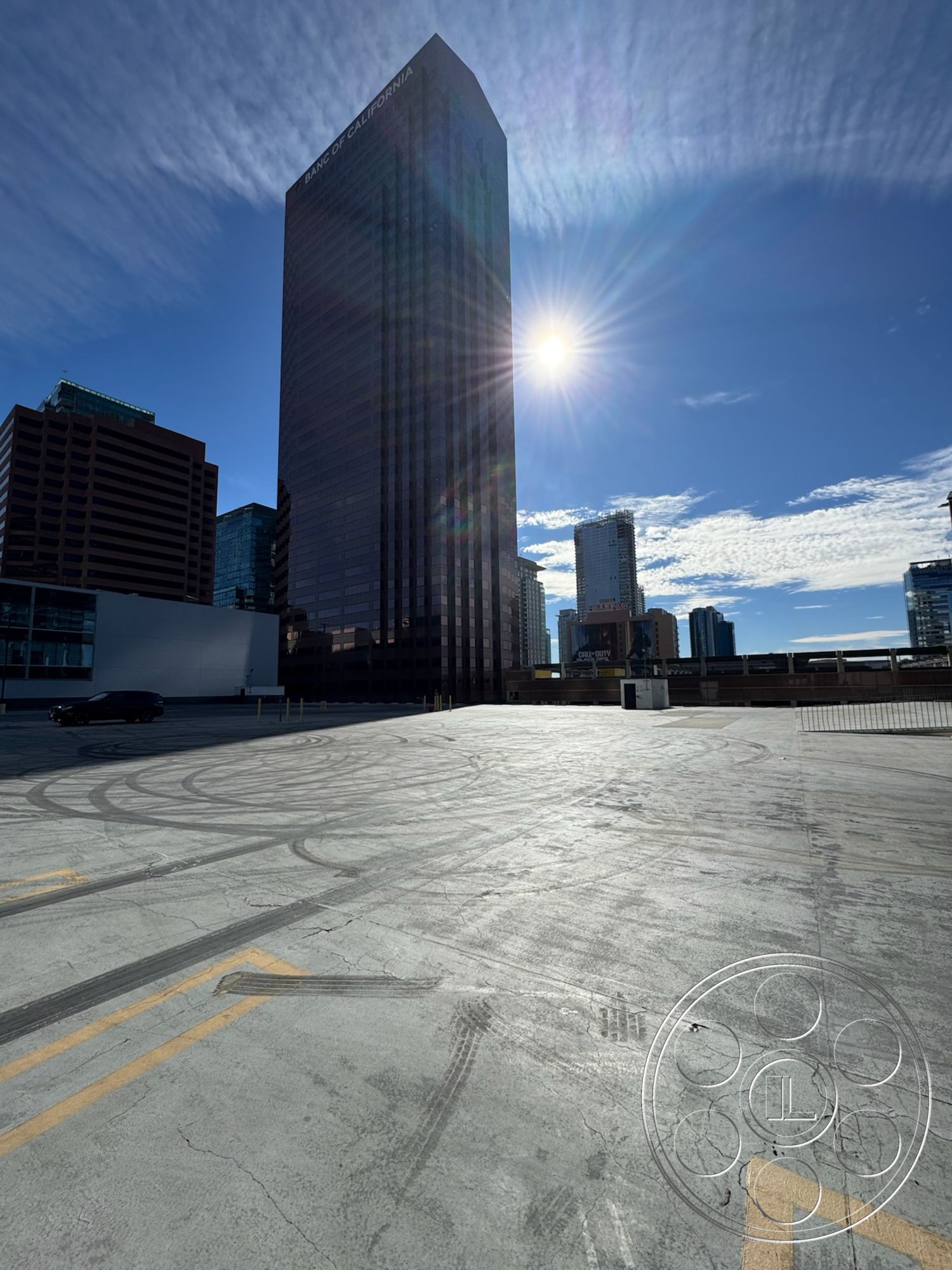 Rooftop 6 - urban landscape, commercial architecture, concrete parking lot surface, open-air parking structure, polished concrete finish, steel structural framework, surrounding skyscrapers, high-rise glass facade building, modern urban skyline, sunlight reflection on glass, exterior city view, asphalt vehicle markings