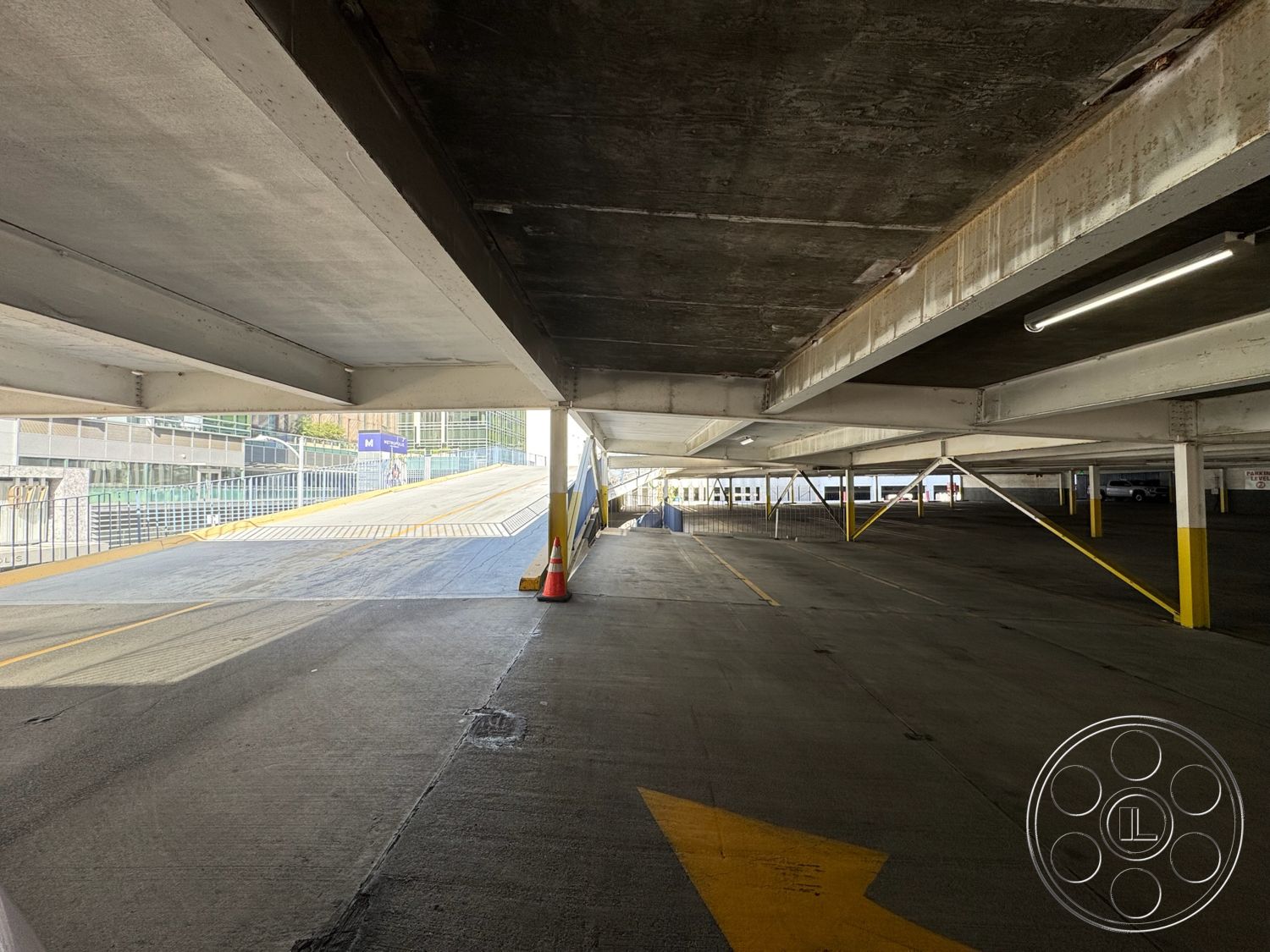 Rooftop 6 - industrial architecture, urban environment, exposed concrete ceiling, linear light fixtures, steel support beams, concrete parking structure walls, concrete parking lot floor, painted concrete columns, asphalt driveway ramp, angled driveway shape, open air parking area, exterior parking layout, spacious parking garage, elevated parking ramp