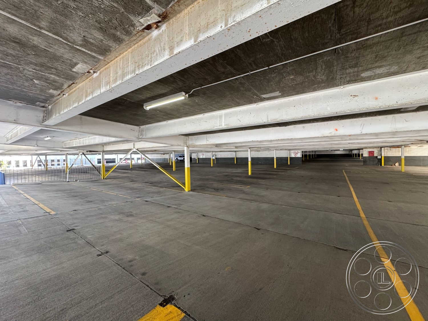 Rooftop 6 - concrete flooring, industrial lighting fixtures, steel support beams, exposed concrete parking garage structure, yellow painted column details, open air parking layout, flat ceiling with concrete finish, interior structure, underground parking level