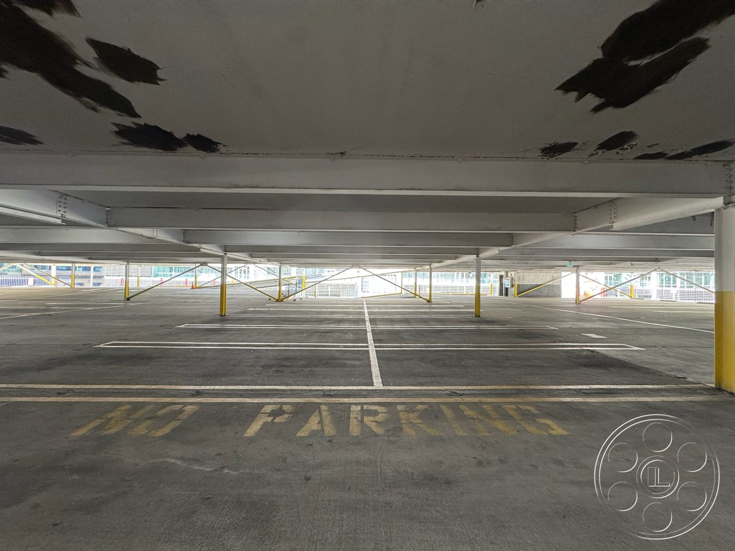 Rooftop 6 - concrete flooring, industrial design elements, minimalist architectural style, steel support beams, urban environment setting, interior parking garage, exposed concrete parking structure, painted concrete ceilings, yellow painted column bases, white painted parking lines, open-air parking lot, structural steel framing