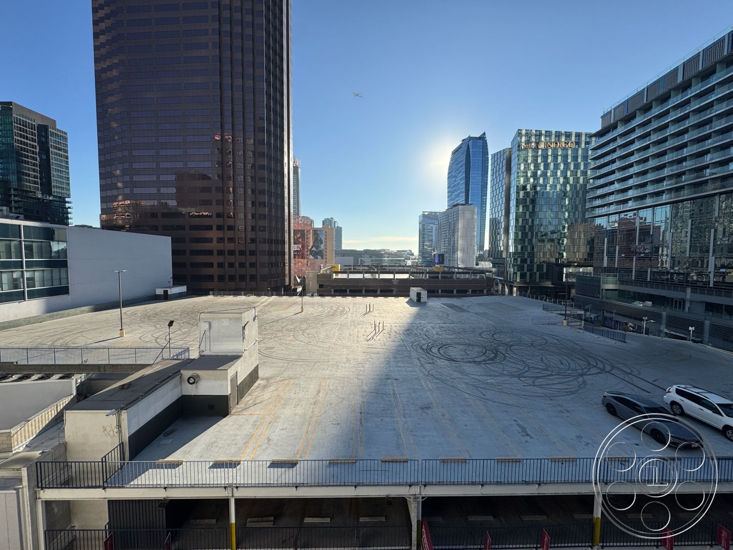 Rooftop 6 - modern architectural style, concrete parking lot, sunlit exterior, commercial building setting, urban city skyline view, polished concrete surface, exposed concrete parking structure, high-rise building background, reflective glass facades, steel railing enclosure, outdoor rooftop space, multi-story urban parking, lower urban environment, suburban cityscape, industrial urban design