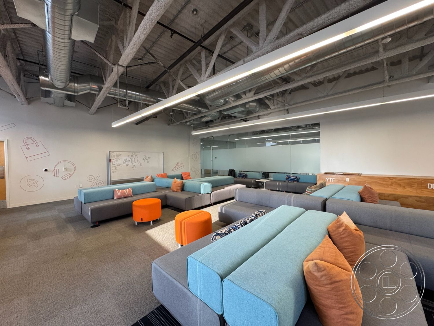 Rooftop 6 - neutral color palette interior, minimalist design aesthetic interior, glass partition walls interior, concrete flooring interior, plush carpet flooring interior, soft seating arrangement interior, exposed metal ductwork interior, modular seating with gray upholstery interior, brightly colored accent cushions interior, industrial ceiling beams interior, functional work area interior, multifunctional lounge space interior, casual collaborative workspace interior