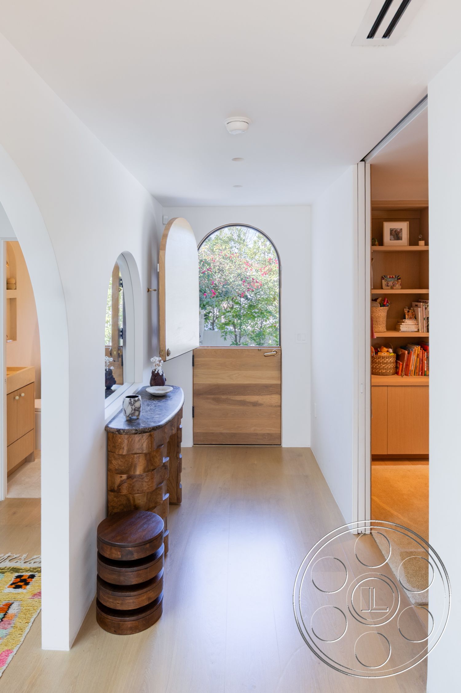 Modern 519 - interior open floor plan, interior hardwood flooring, natural wood console table, interior warm color palette, interior arched doorways, interior decorative wall mirror, interior minimalist design aesthetics, interior soft natural light, interior custom wood cabinetry, interior round wooden stools, interior smooth white walls, interior ambient ceiling lighting, interior large arched window, interior textured decorative rug